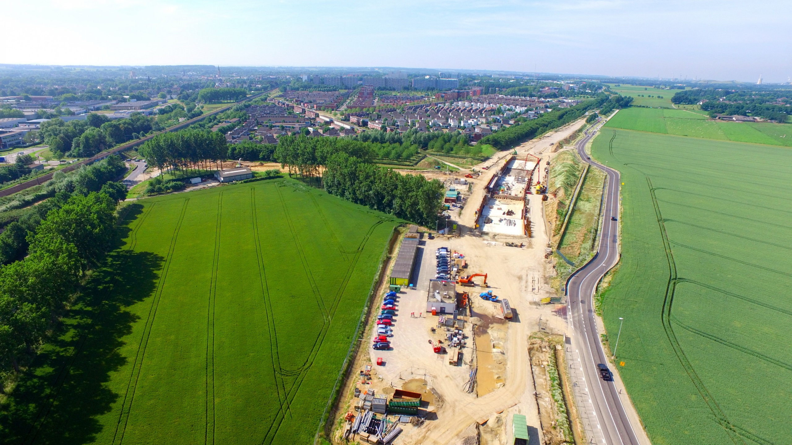 Dronefoto van een bouwplaats met een weg ernaast en een dorp op de achtergrond
