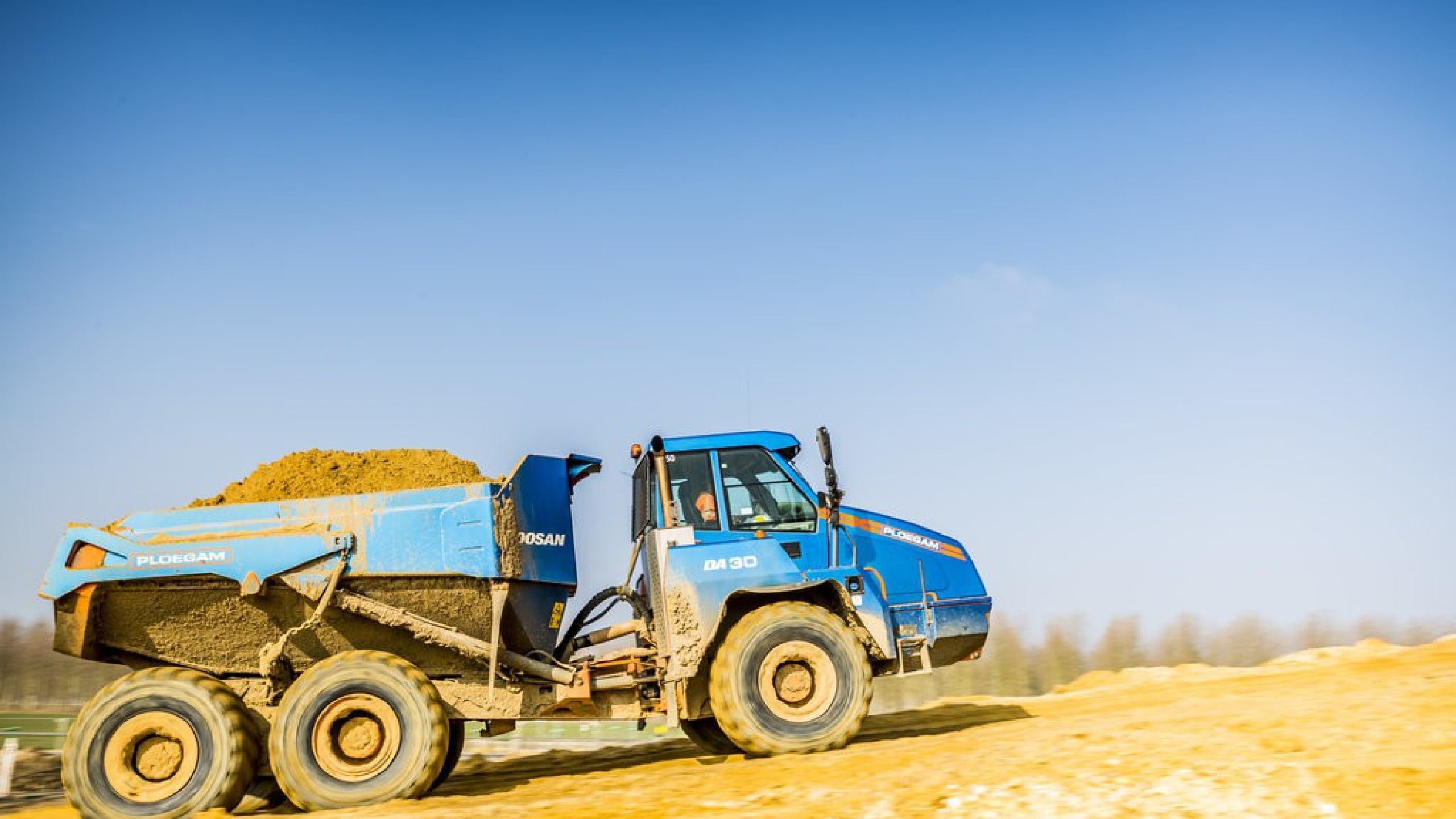 Bak van blauwe Ploegam vrachtwagen gevuld met zand rijdt over het zand