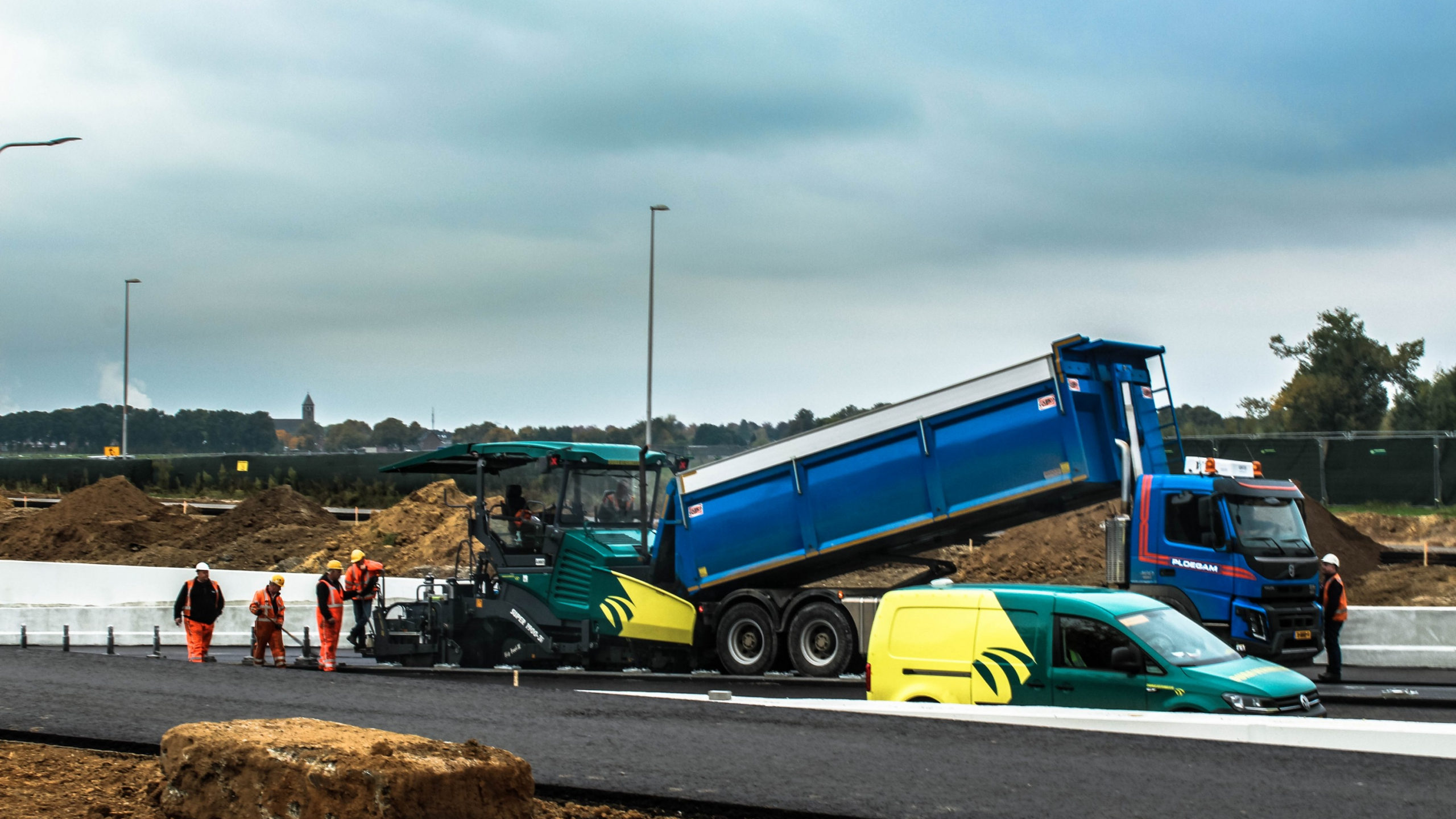 Ploegam vrachtwagen en Dura Vermeer bus en tractor staan op een weg met bouwvakkers erbij