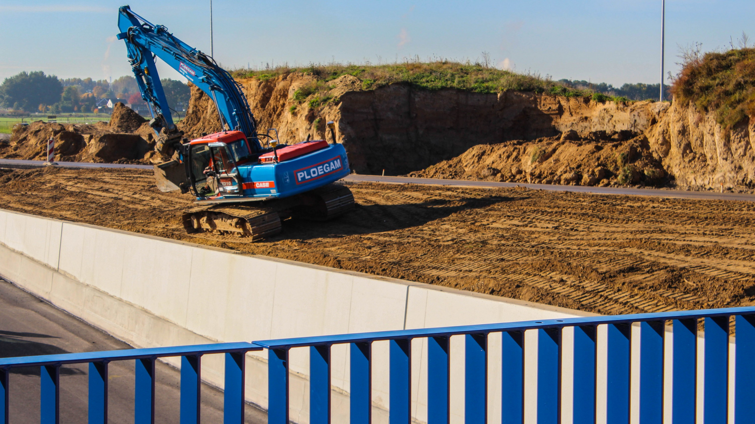 Blauwe Ploegam vrachtwagen aan het werk in het zand met een blauw hek op de voorgrond