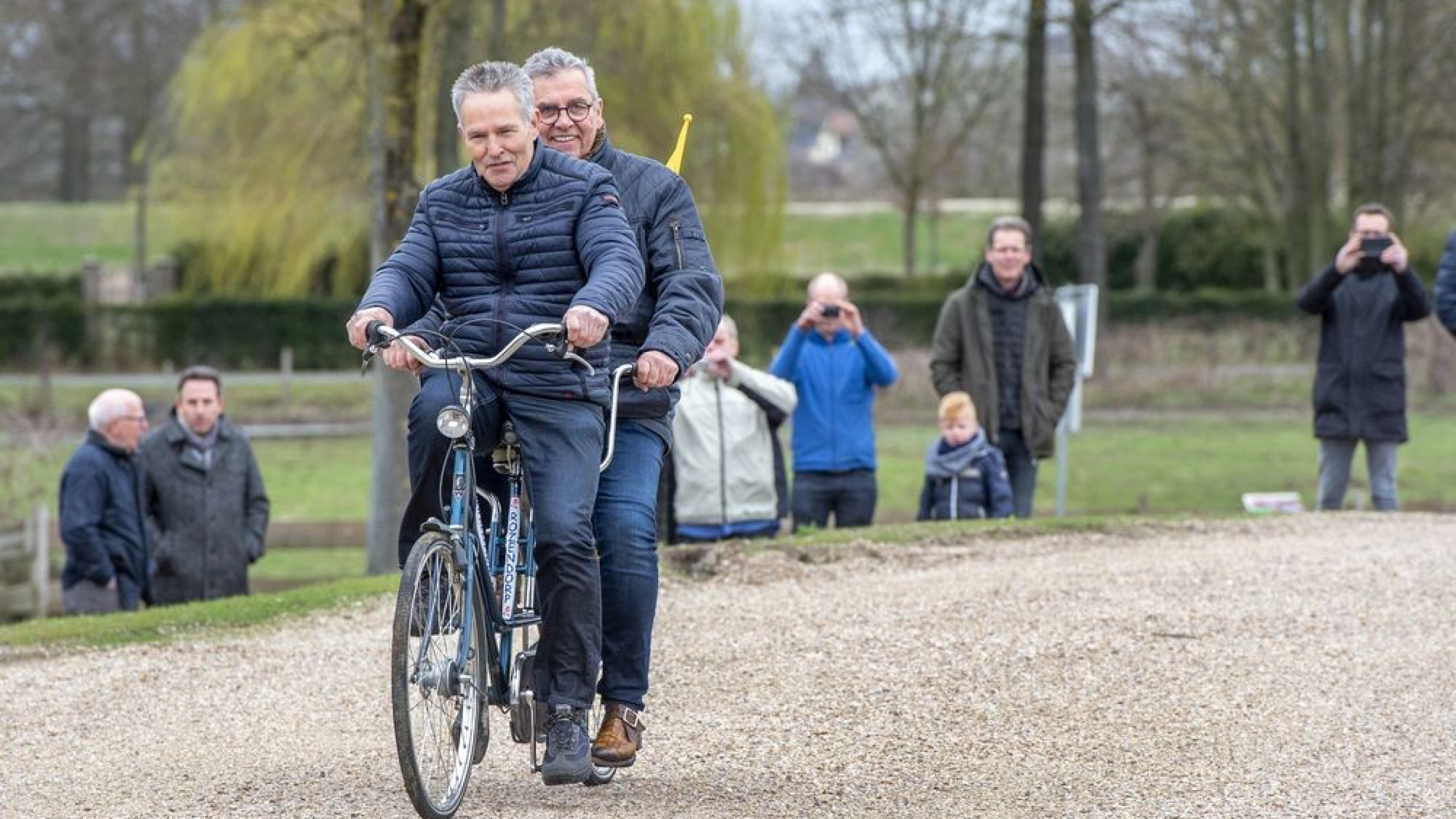 Twee personen fietsen op tandem met toeschouwers naast de weg