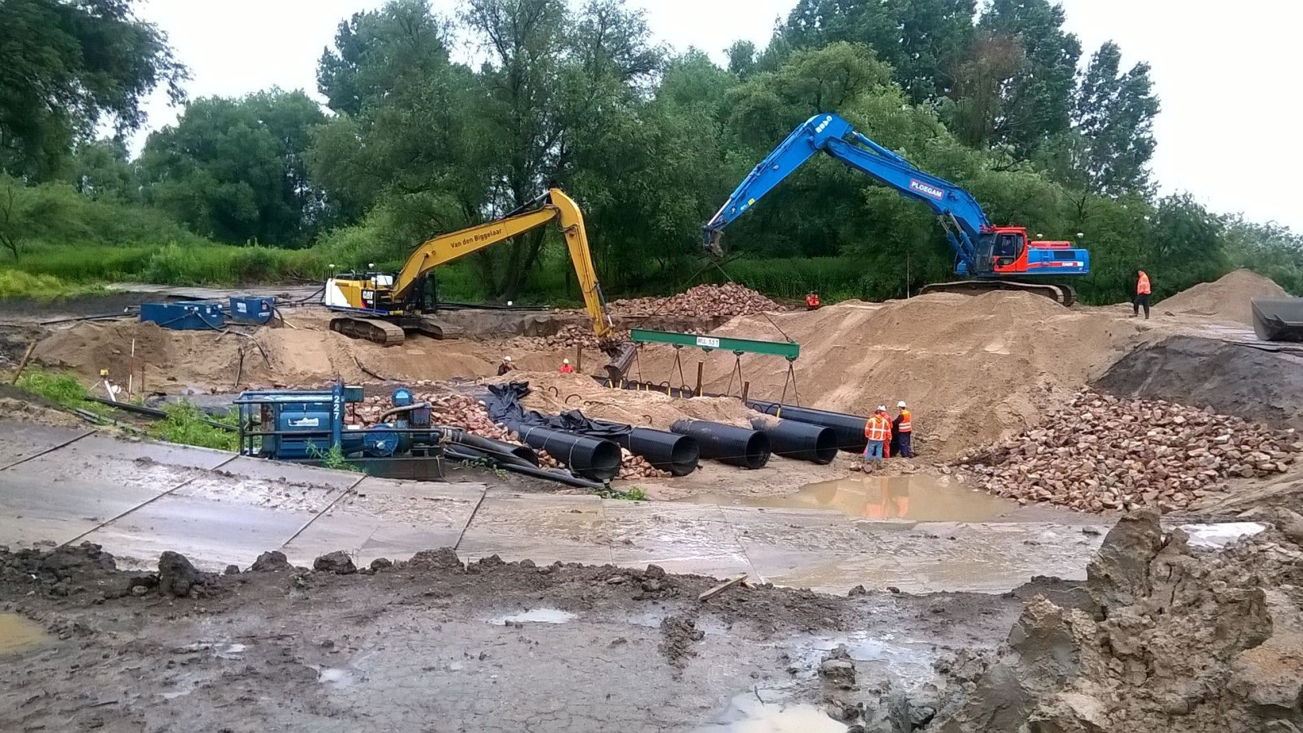 Blauwe Ploegam kraan en gele kraan aan het werk tussen zand en stenen