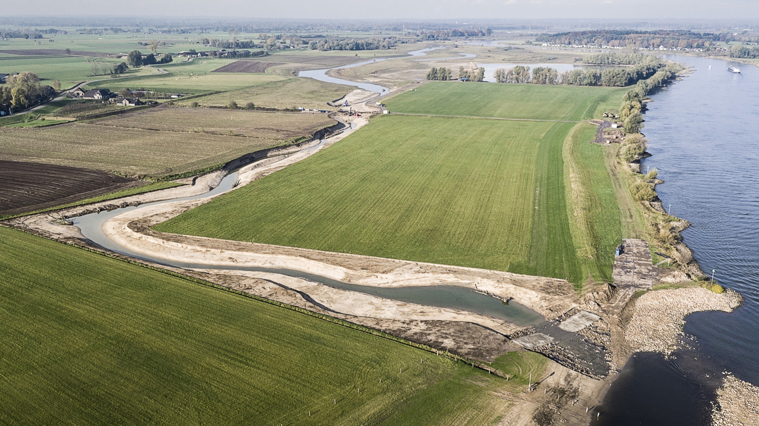 Luchtfoto van natuurgebied naast de IJssel waar een beekje tussen groene weilanden stroomt