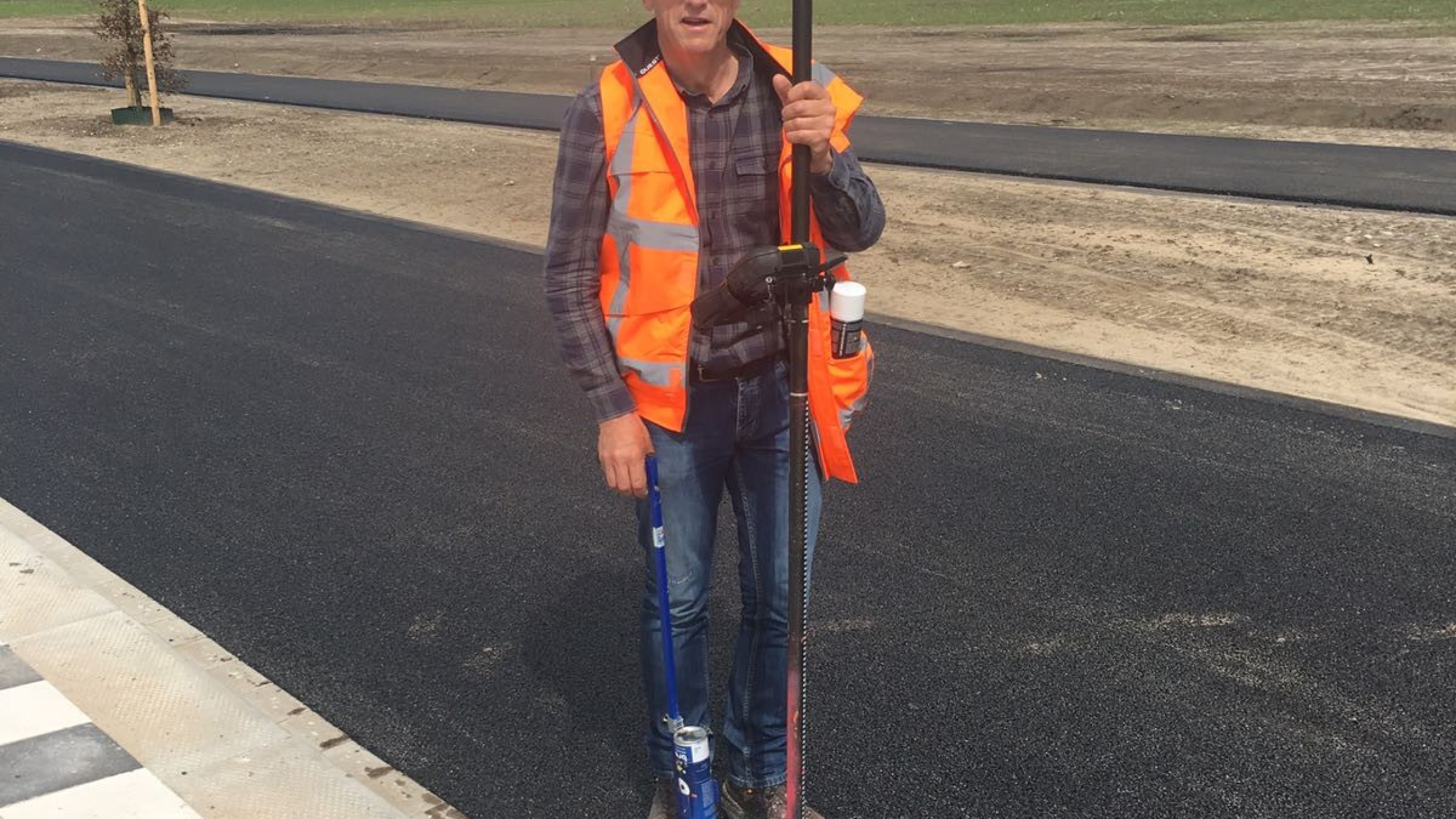 Man met oranje veiligheidshesje op straat met meetapparatuur