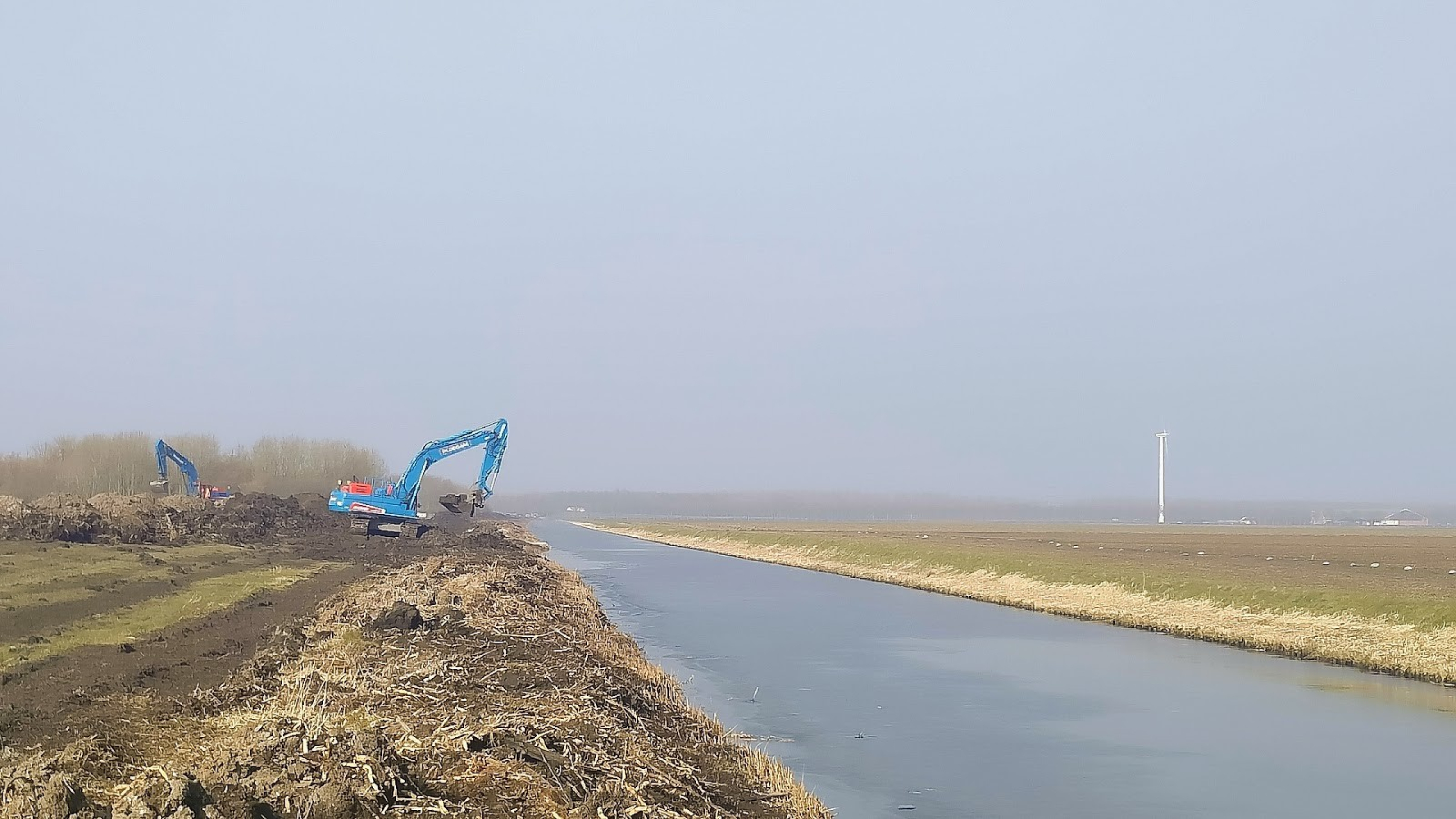 Blauwe Ploegam kraan aan het werk naast een rivier