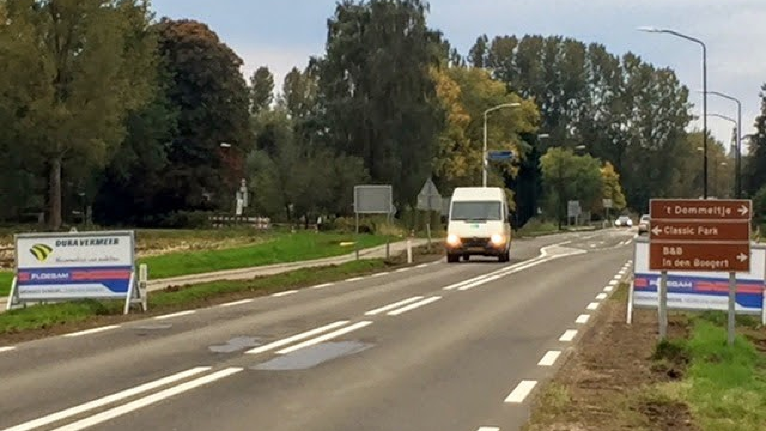 Witte bus rijdt over weg met borden ernaast