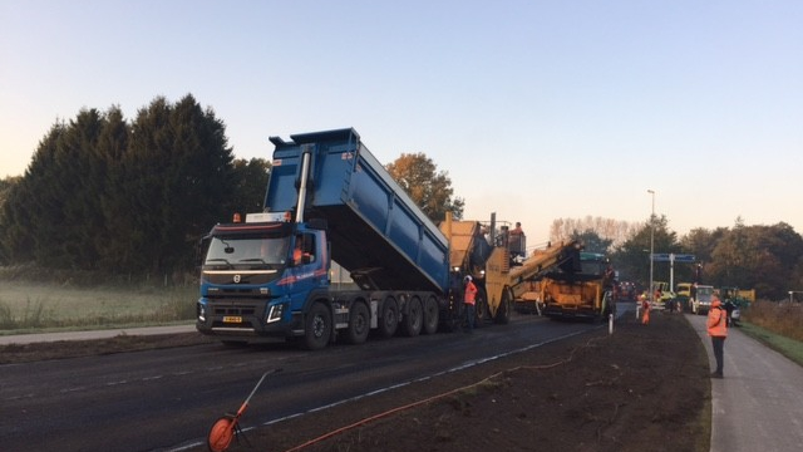 Blauwe Ploegam vrachtwagen staat op de weg met bouwvakkers in oranje hesjes