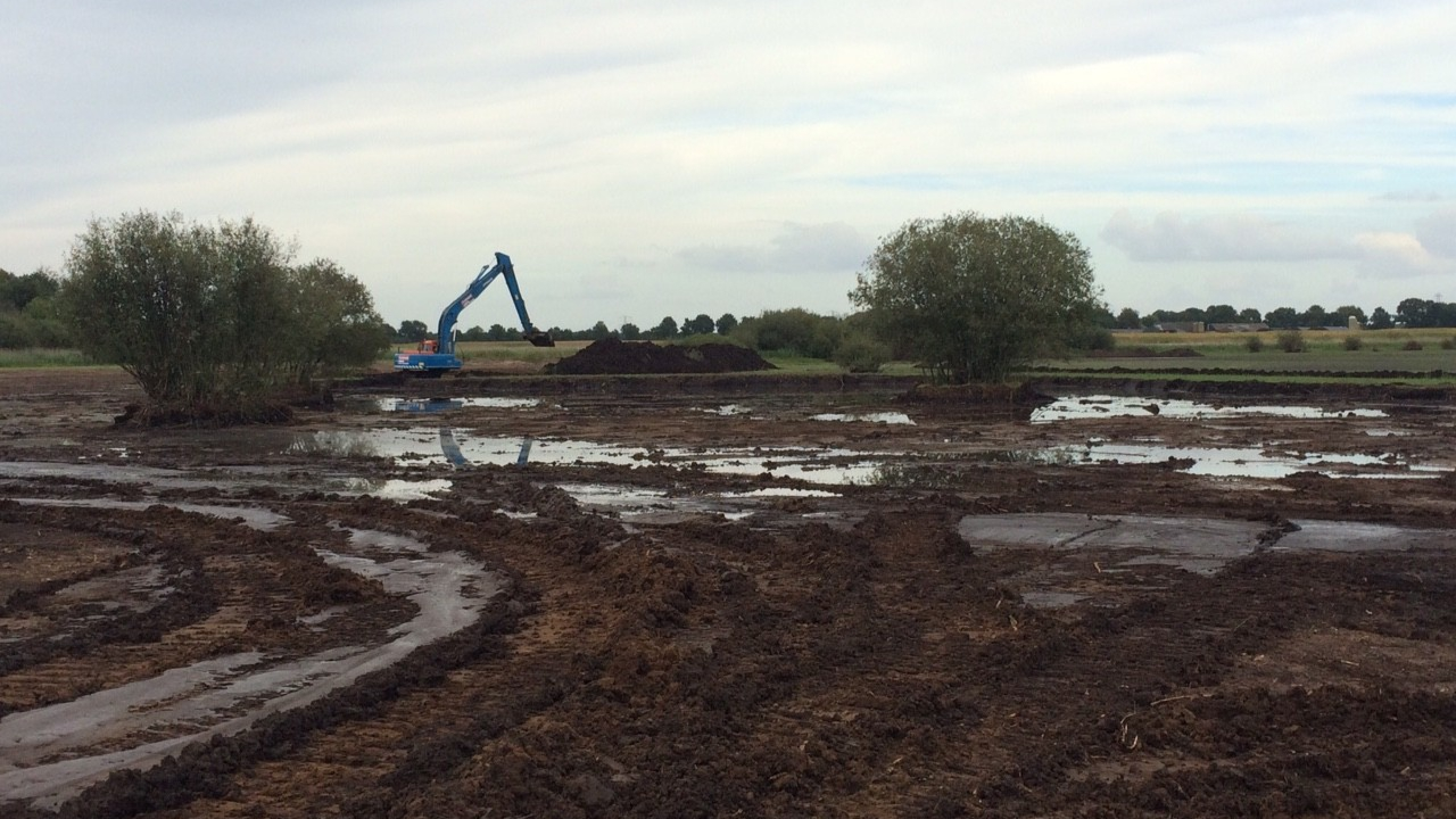 Blauwe Ploegam kraan aan het werk in een natuurgebied met veel regenplassen en modder
