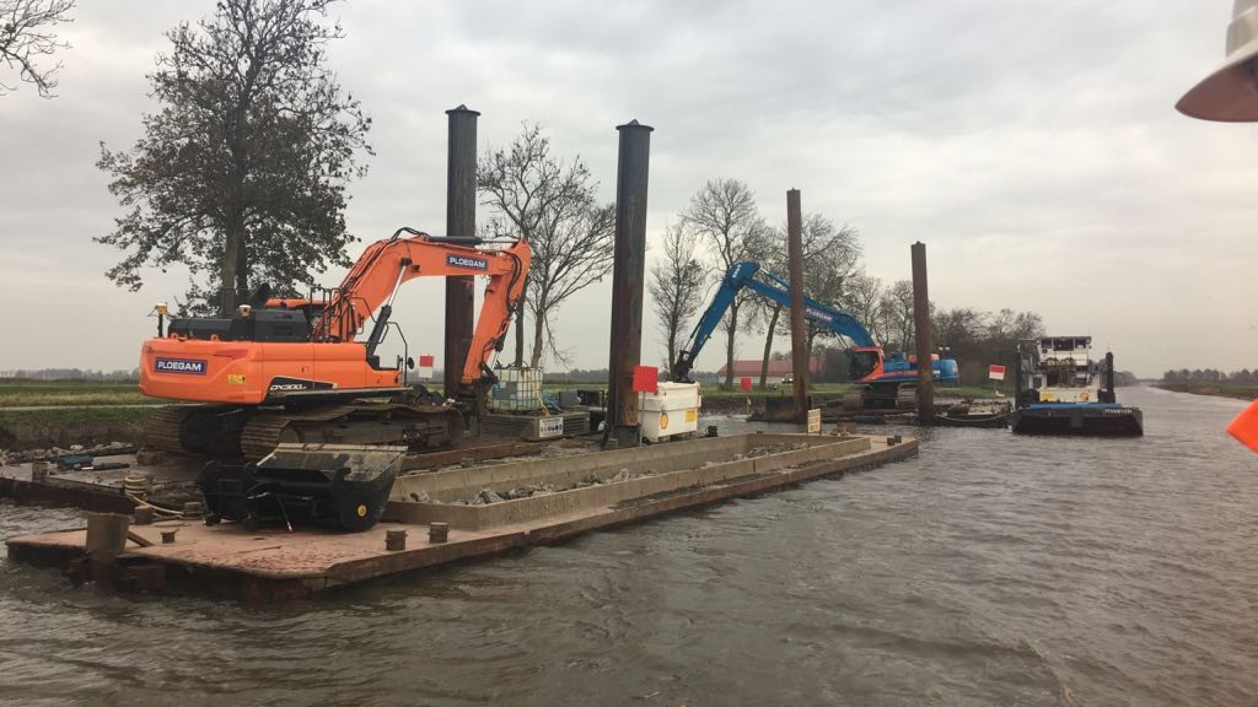 Oranje kraan en blauwe Ploegam kraan werken op ponton vanaf het water