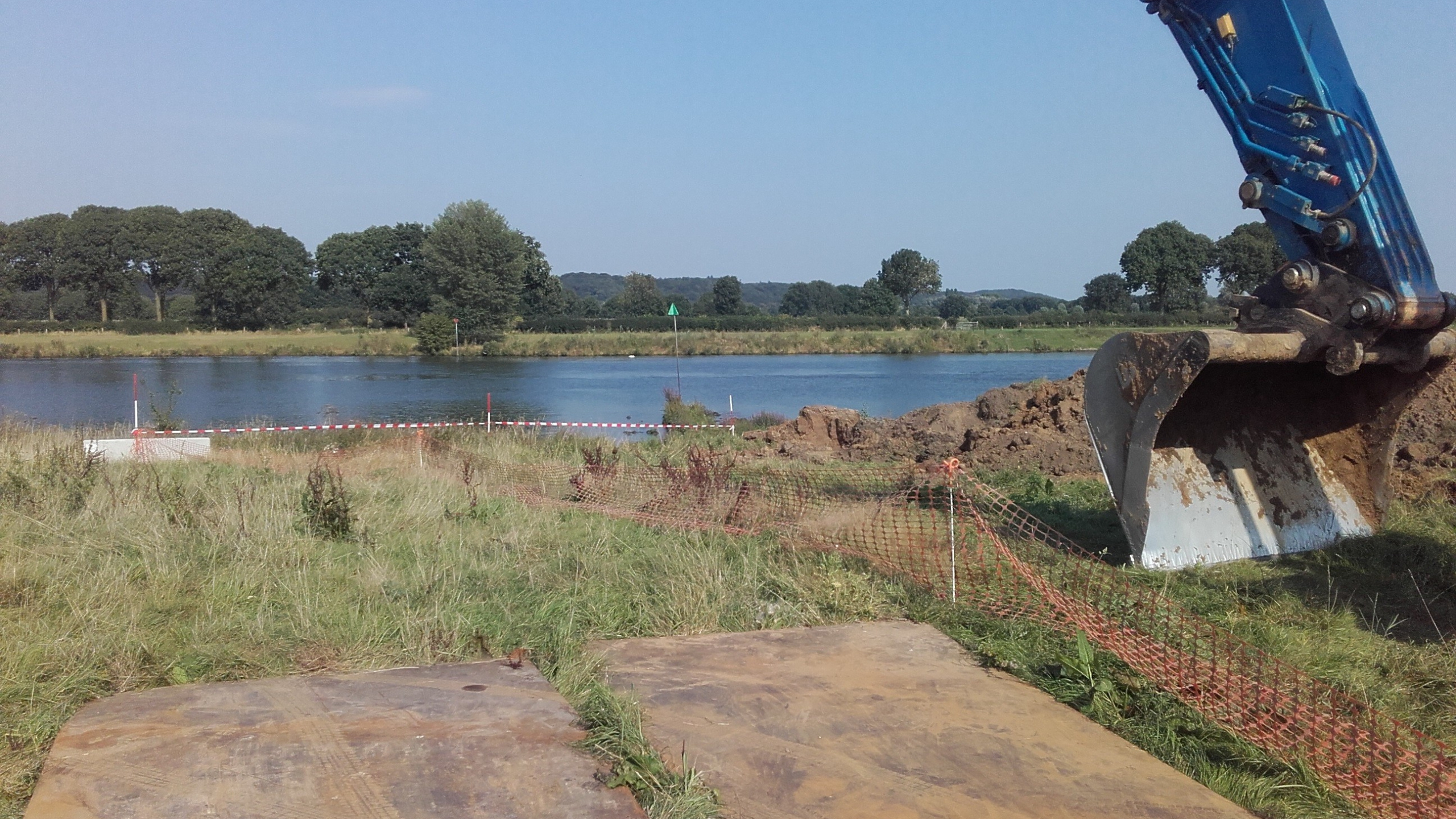 Bak van blauwe kraan bij werkzaamheden naast een rivier
