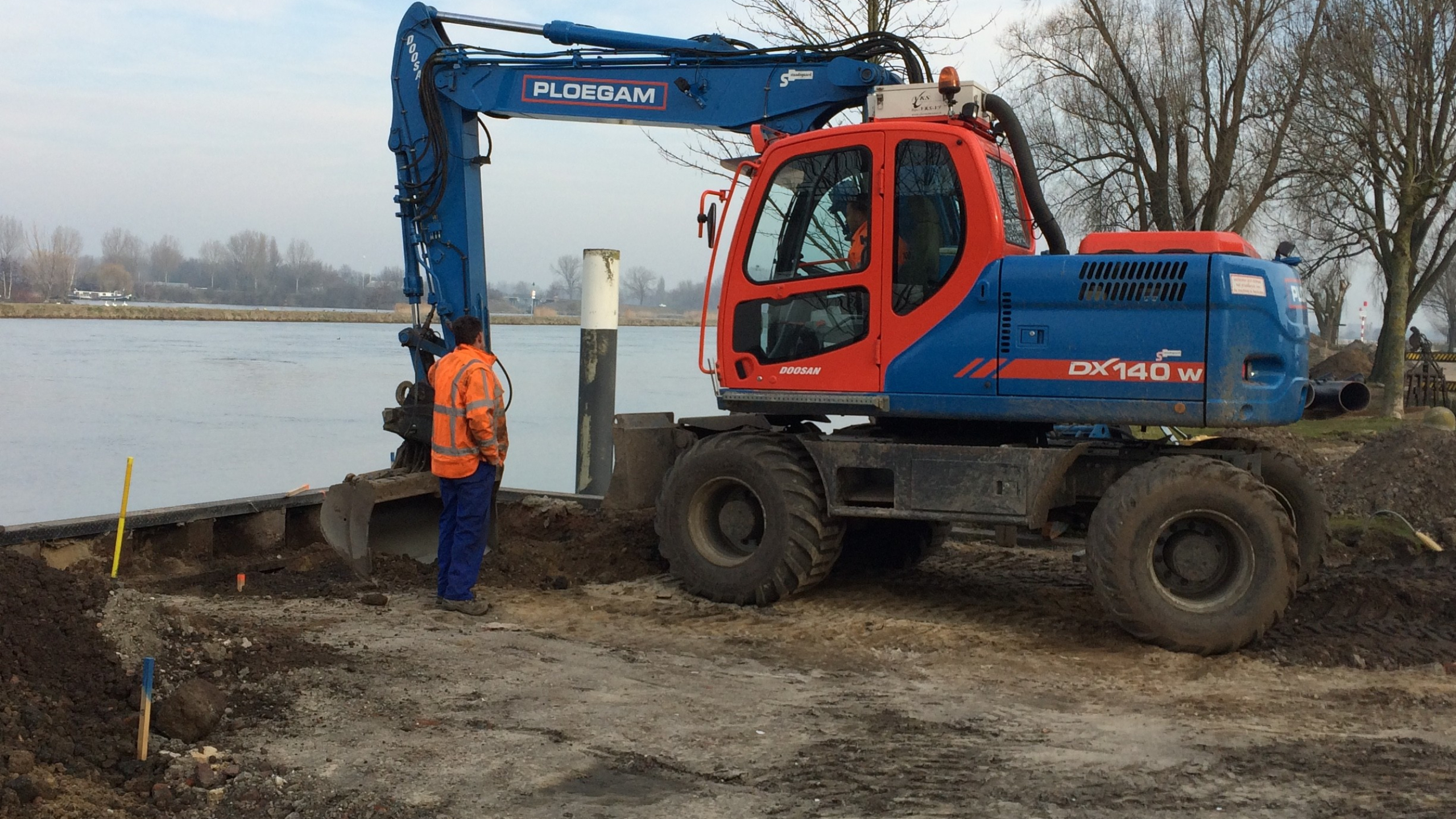 Blauwe Ploegam graafmachine in het zand naast een rivier