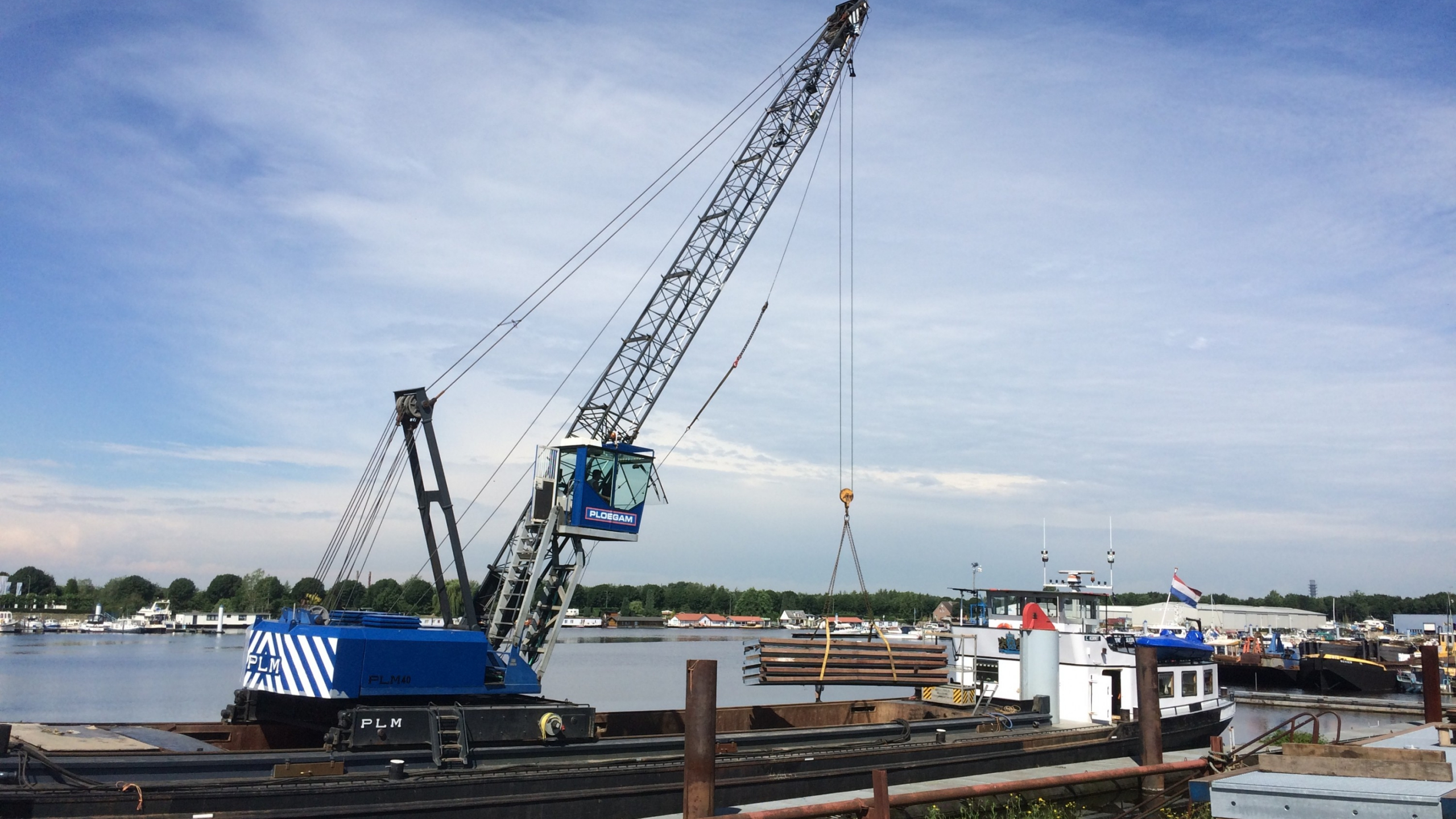 Blauwe Ploegam kraan plaatst damwanden vanaf een schip