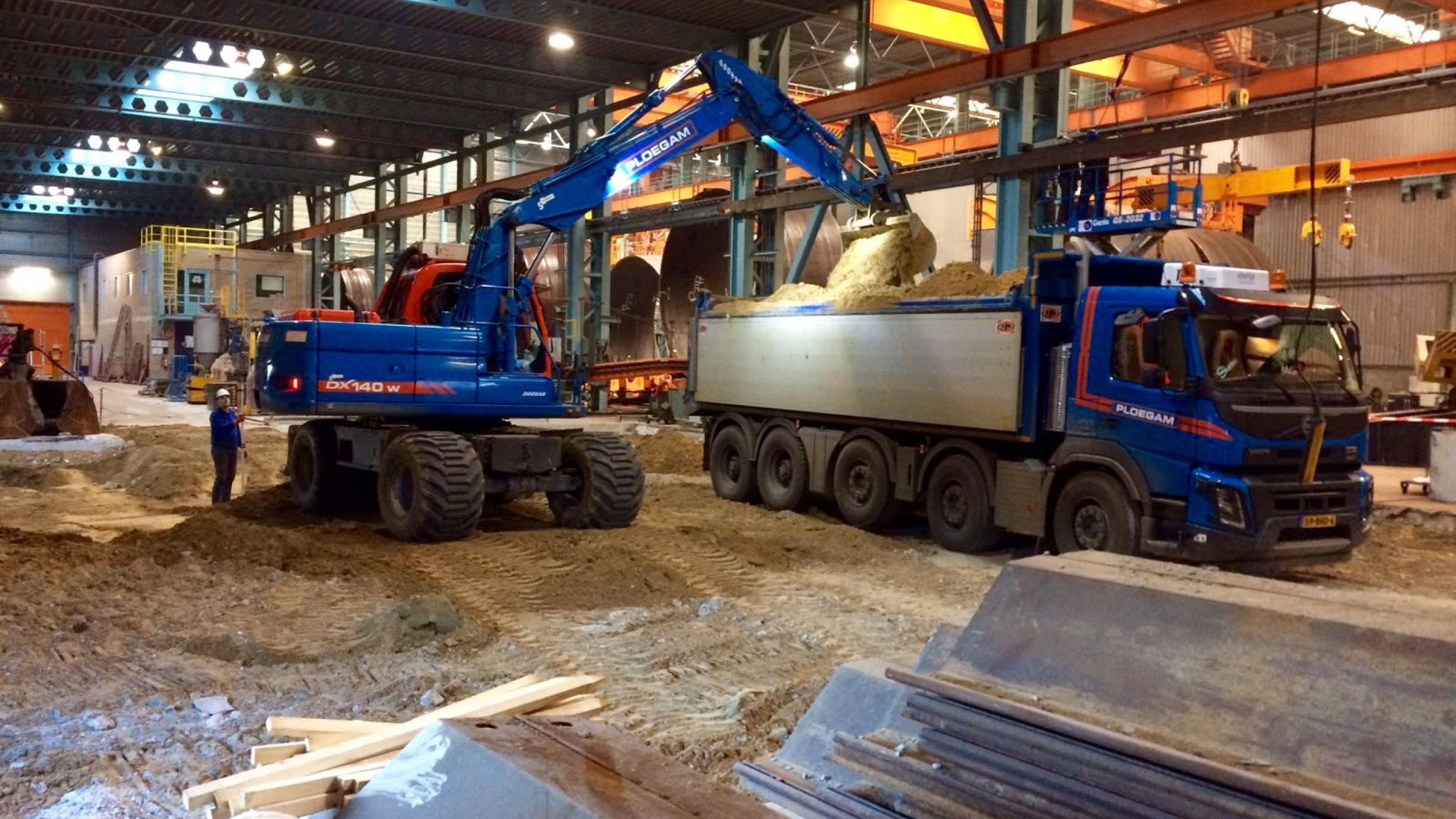 Blauwe kraan schept zand in Ploegam vrachtwagen in een loods