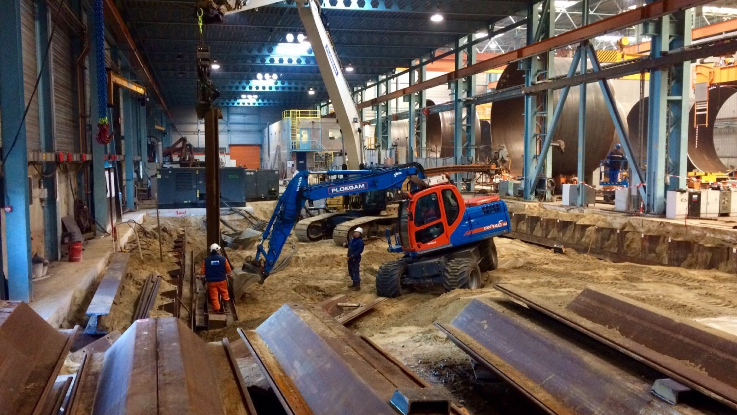 Ploegam kraan aan het werk bij een bouwkuip in een loods