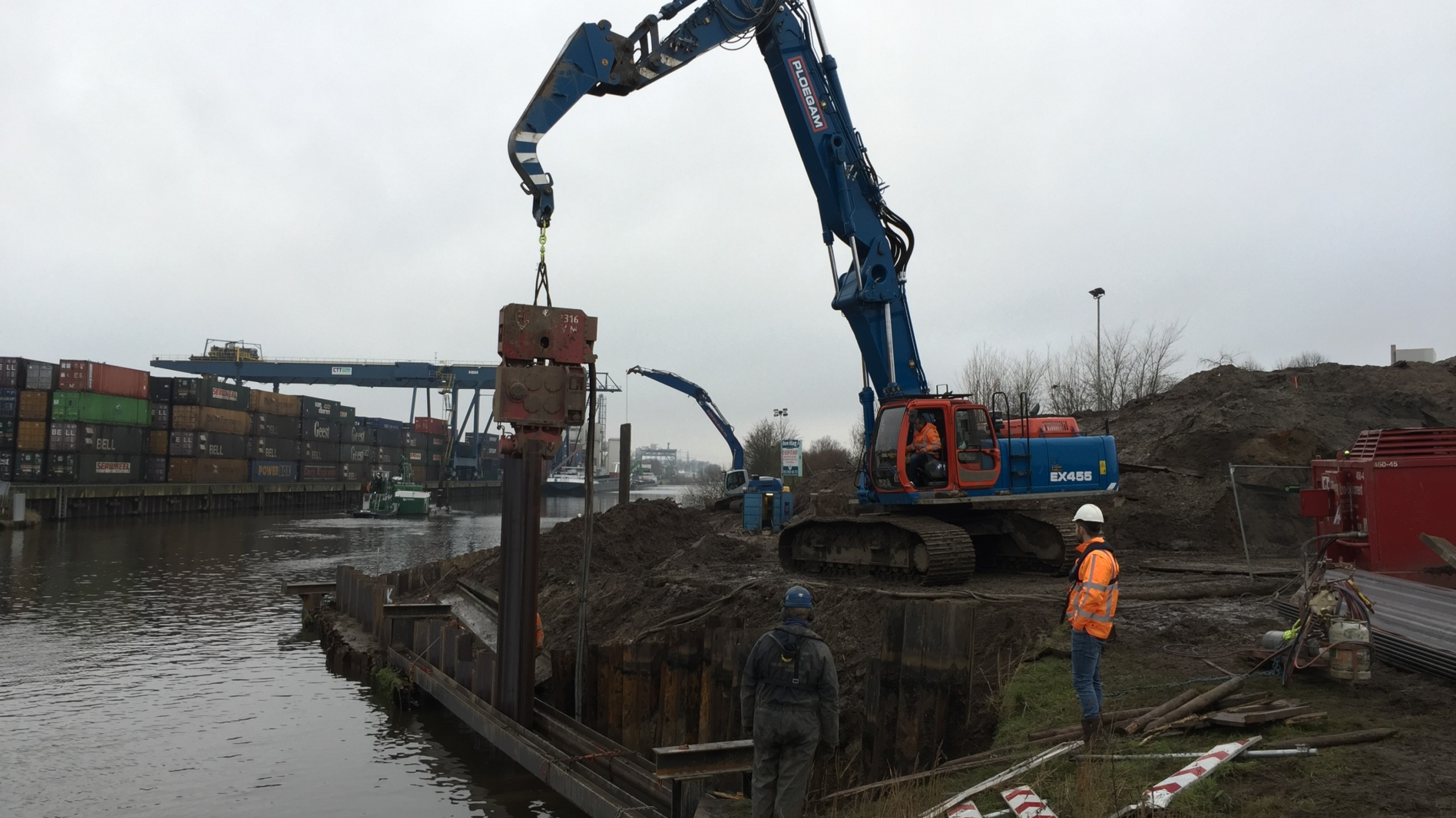 Medewerker Ploegam met veiligheidsjas kijkt naar een kraan die damwand plaatst 