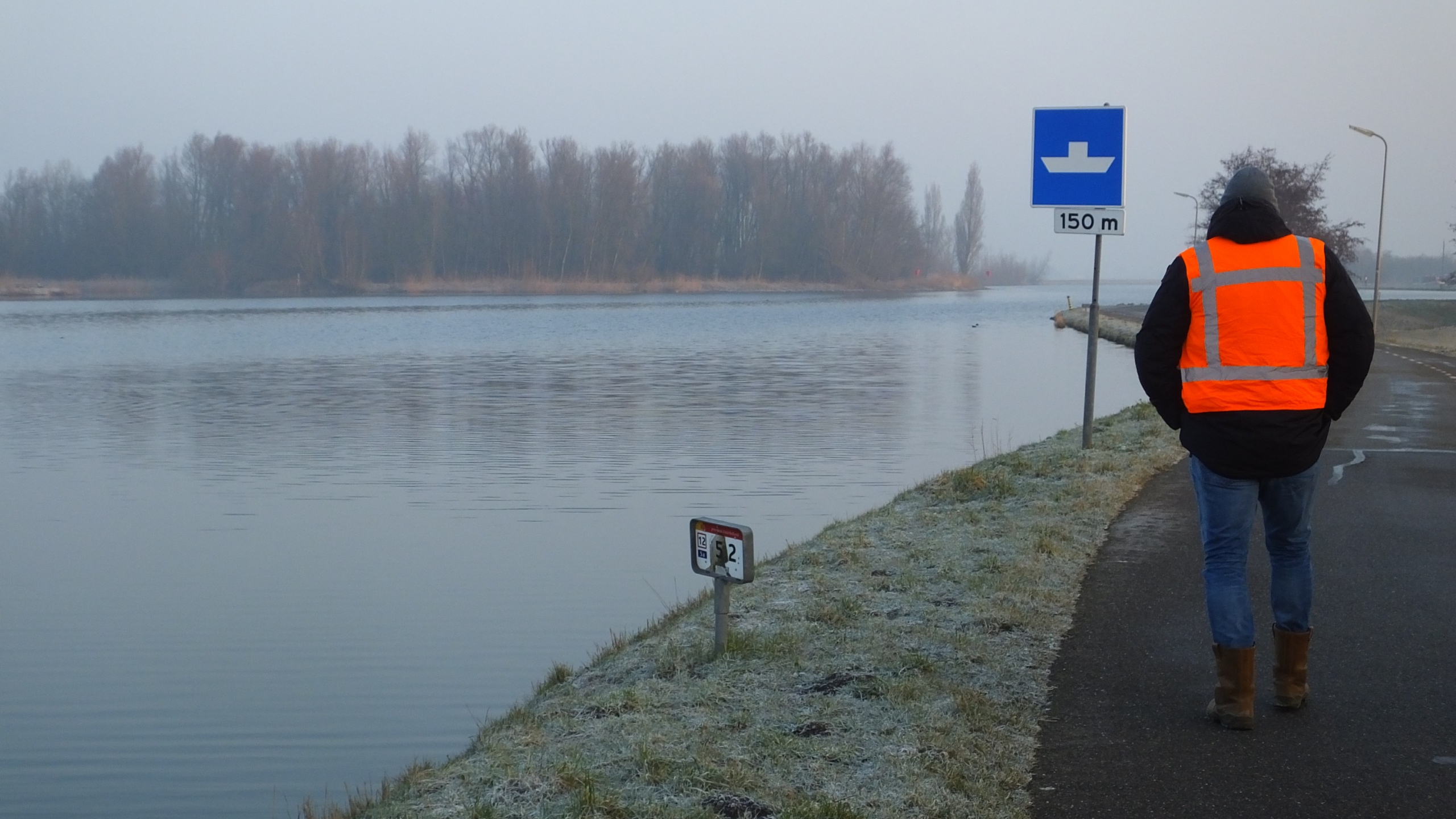 Man met oranje veiligheidshesje loopt op weg naast het water in de Boterhuispolder