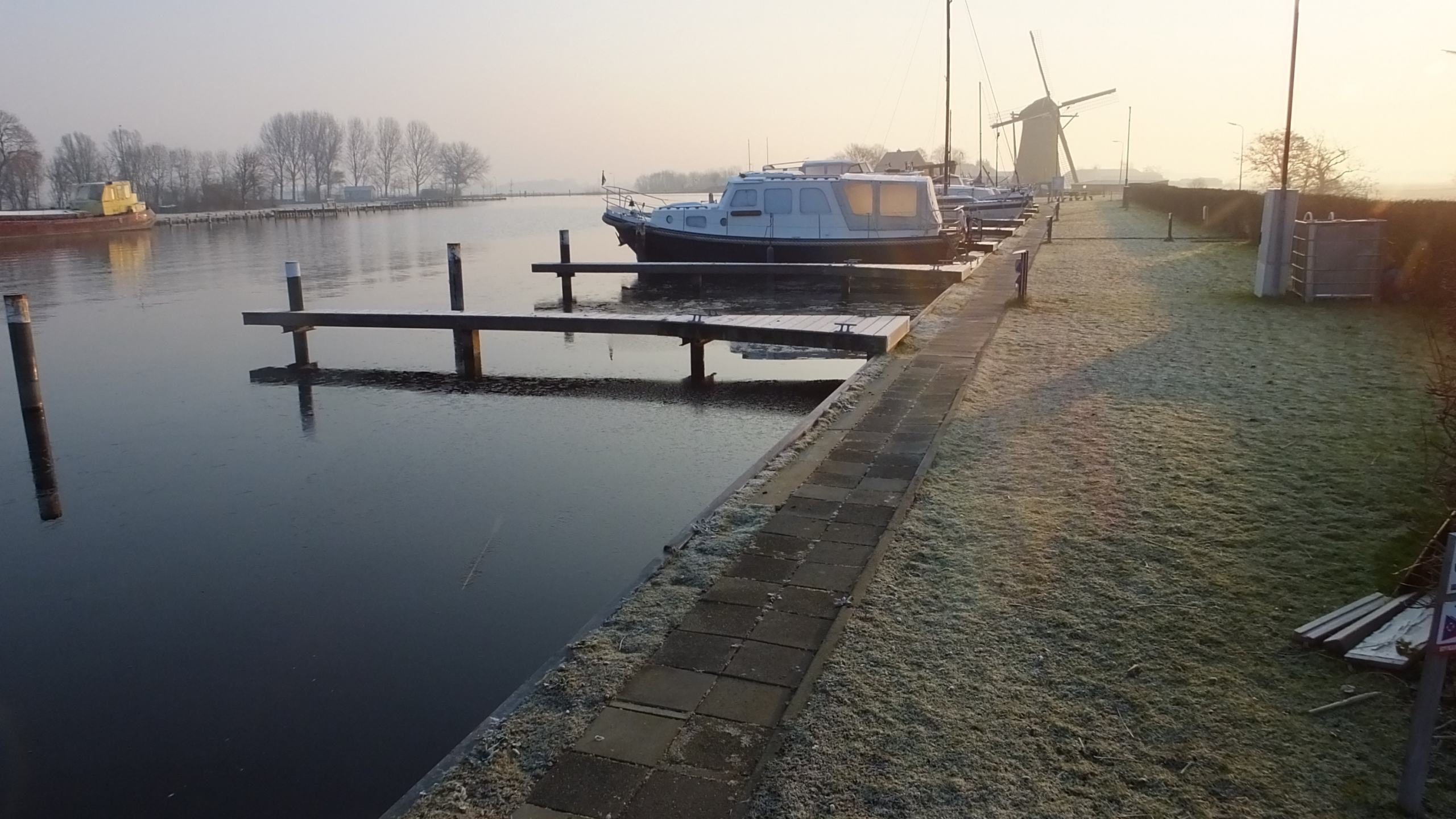 Zonopkomst in een kleine haven met molen op de achtergrond