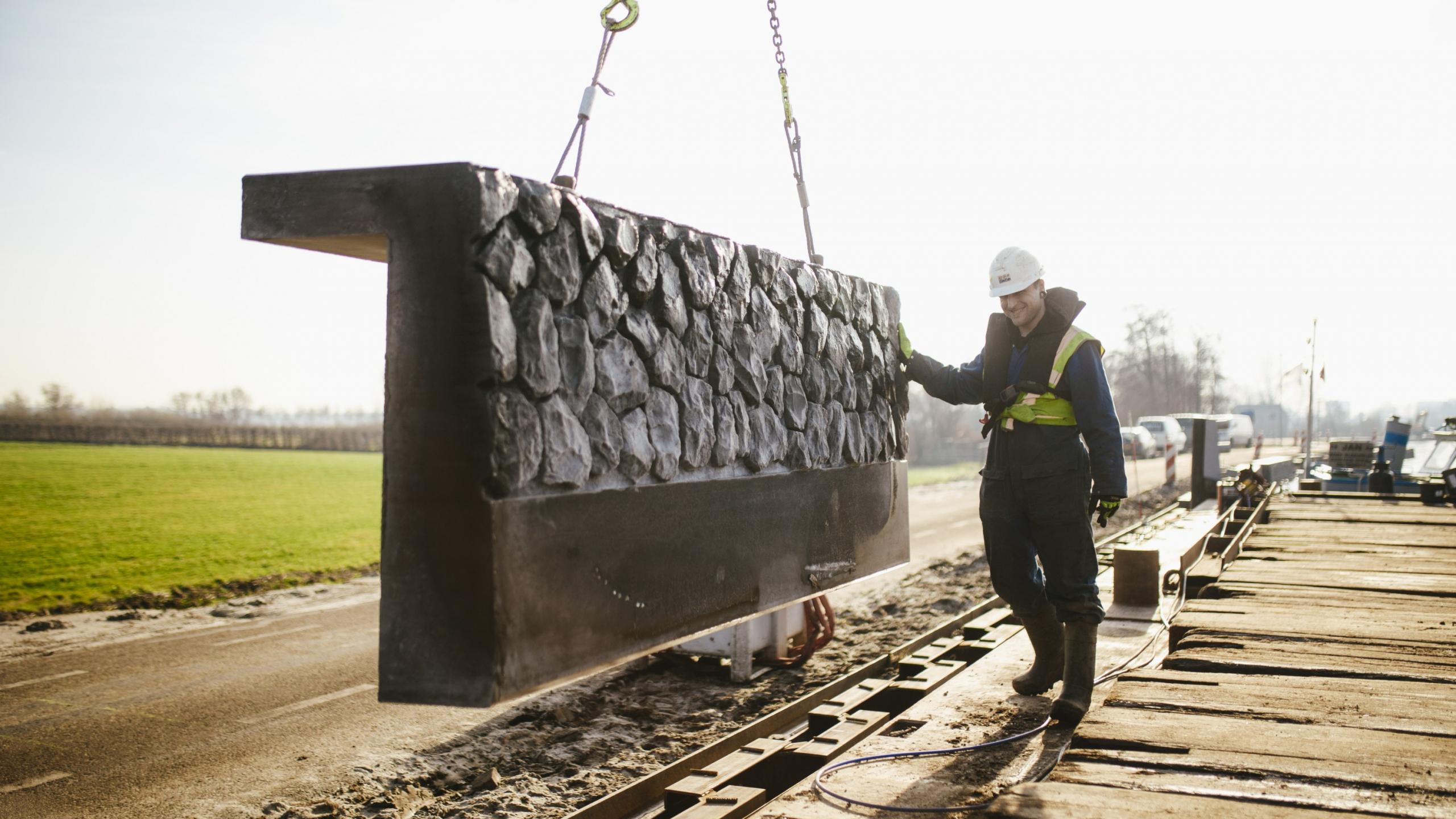 Man met witte helm begeleidt beton met stenen in de grond in de Boterhuispolder