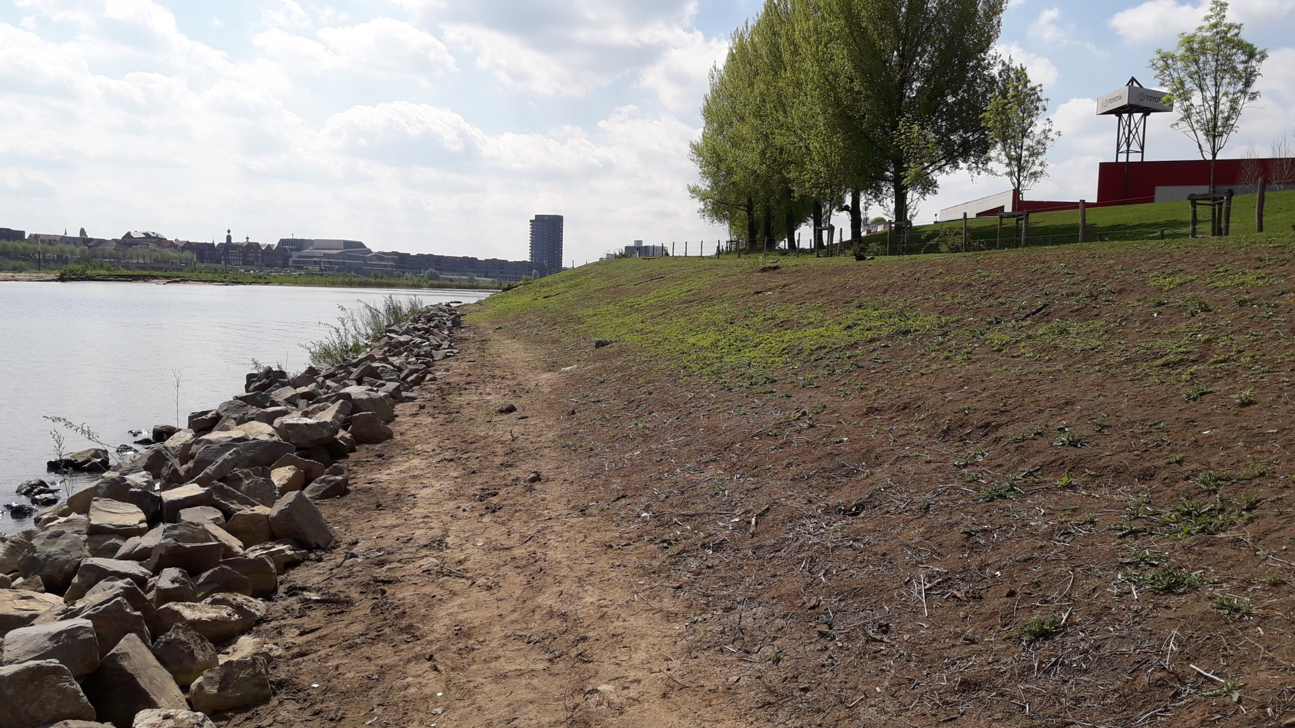 Dijk van zand en gras naast rivier met stad op de achtergrond