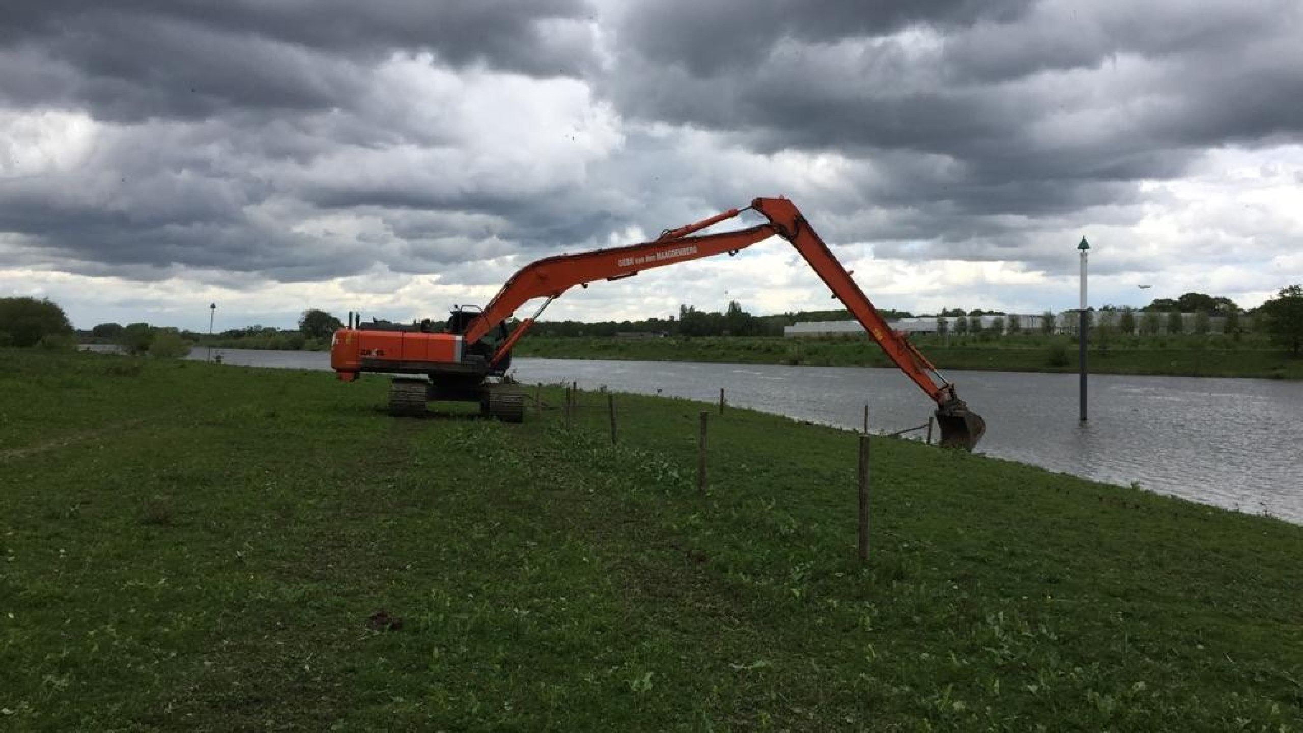 Oranje kraan met lange giek op het gras naast een rivier