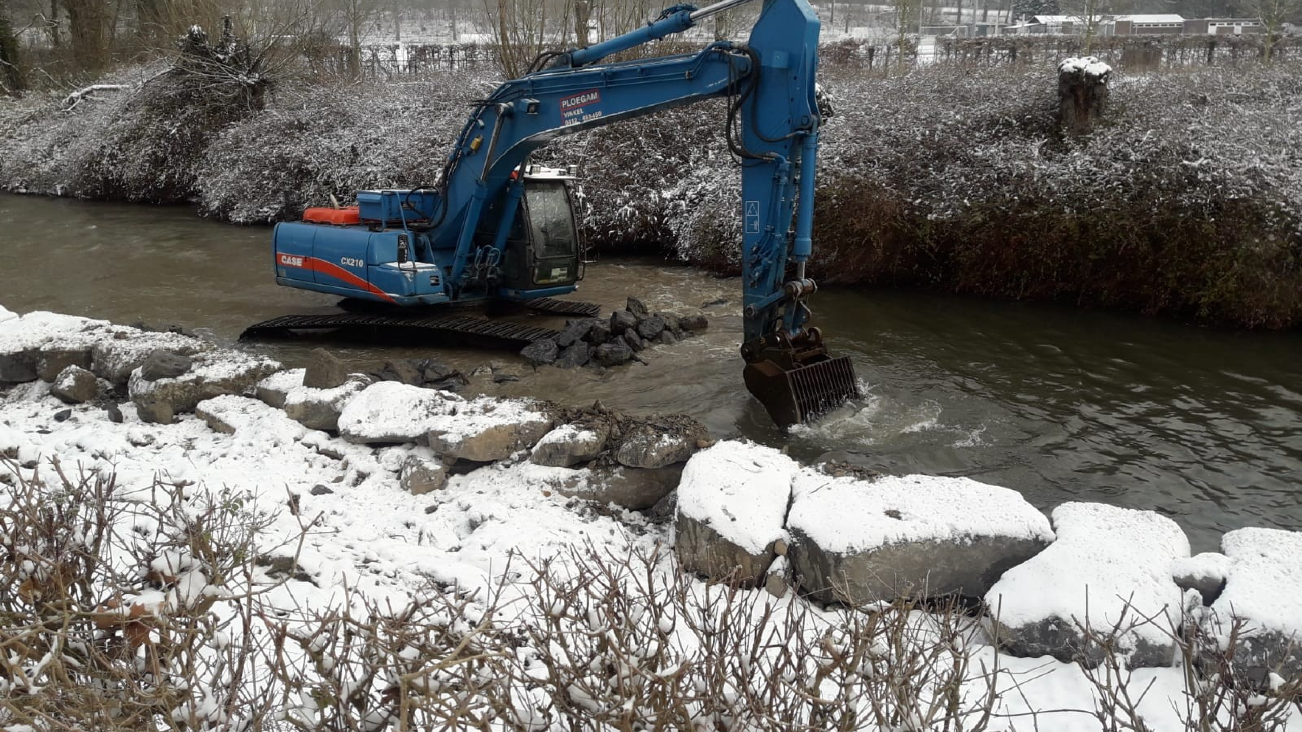 Blauwe Ploegam kraan aan het werk in het water met sneeuw op de kade