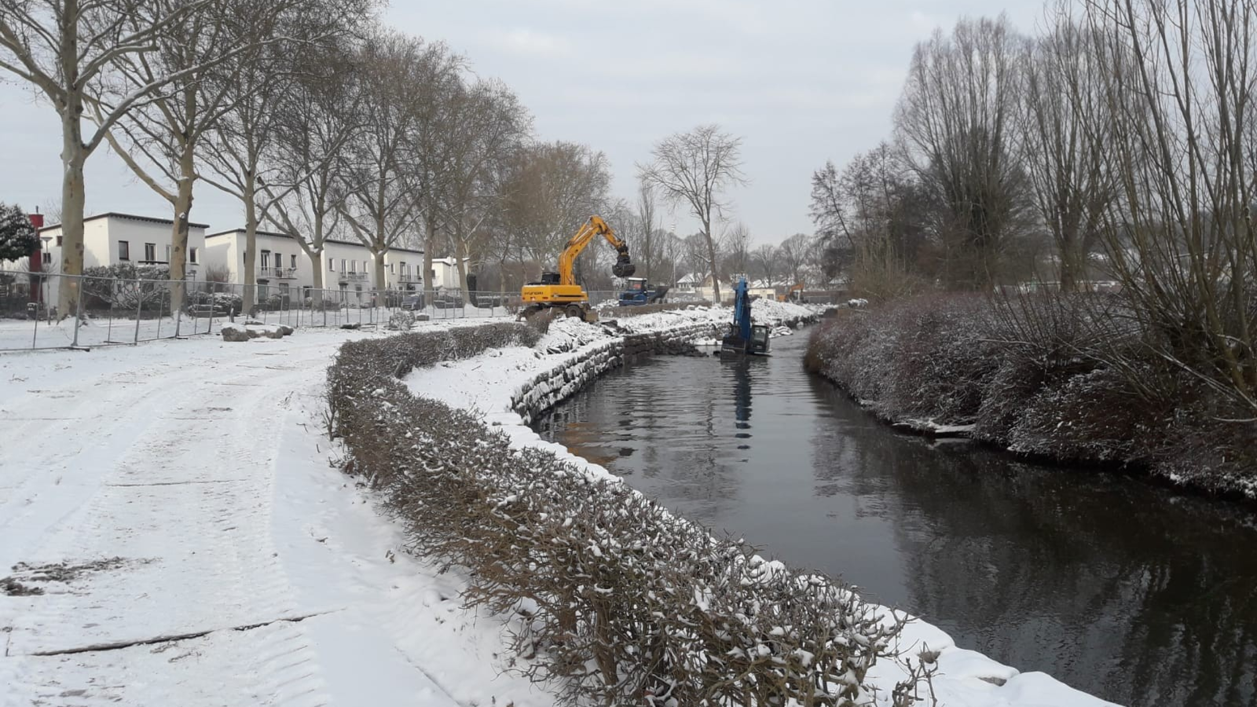 Gele kraan aan het werk naast beek in de sneeuw