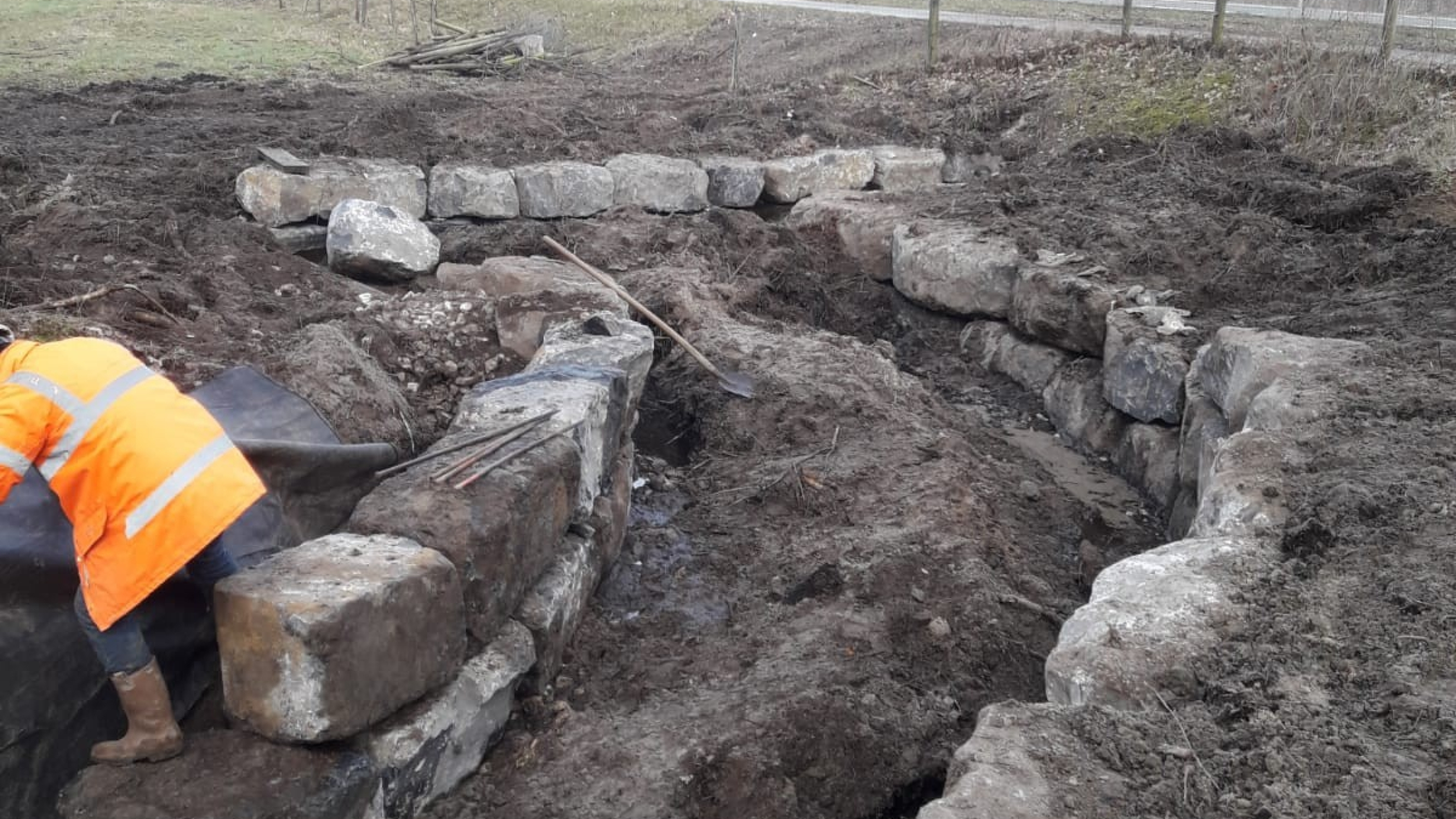 Man met oranje veiligheidsjas aan het werk bij stapelmuur van stenen
