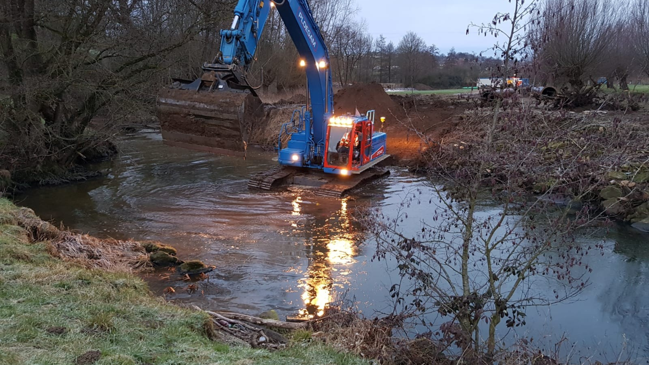 Blauwe Ploegam kraan aan het werk in een beek in de schemering met de lampen aan