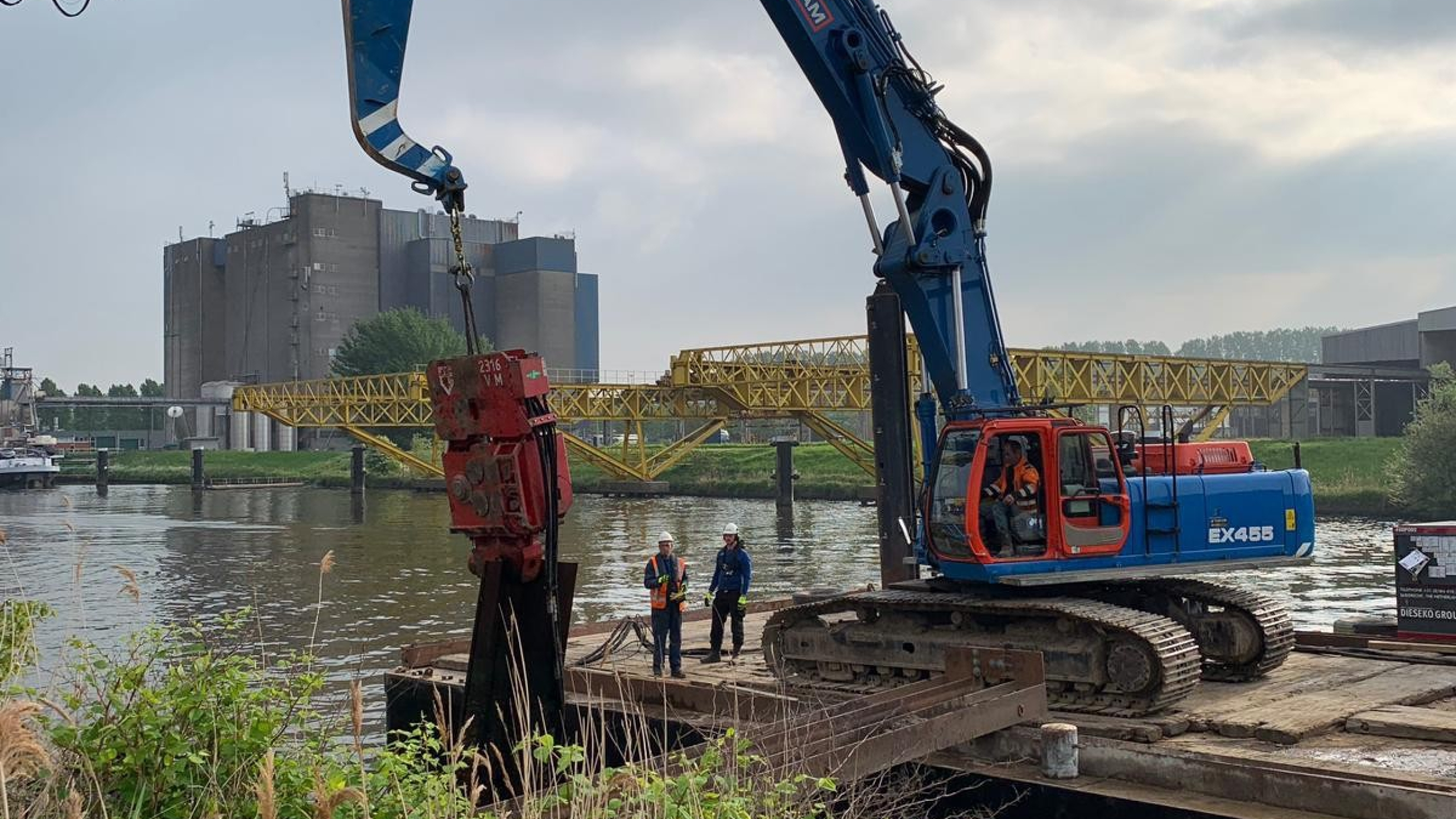 Blauwe Ploegam kraan hijst damwand vanaf een ponton in het water