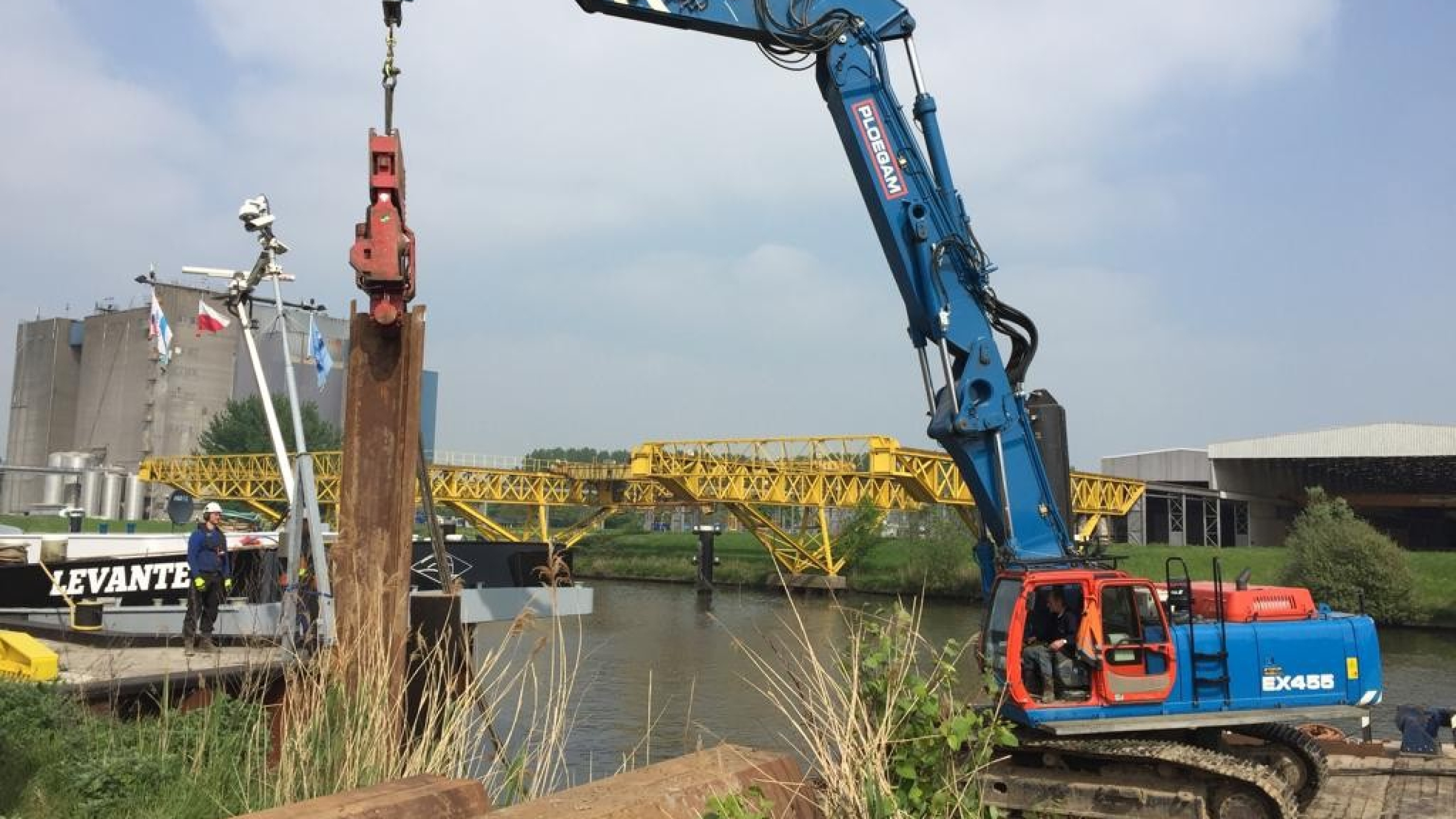 Blauwe Ploegam kraan hijst damwand vanaf een ponton in het water