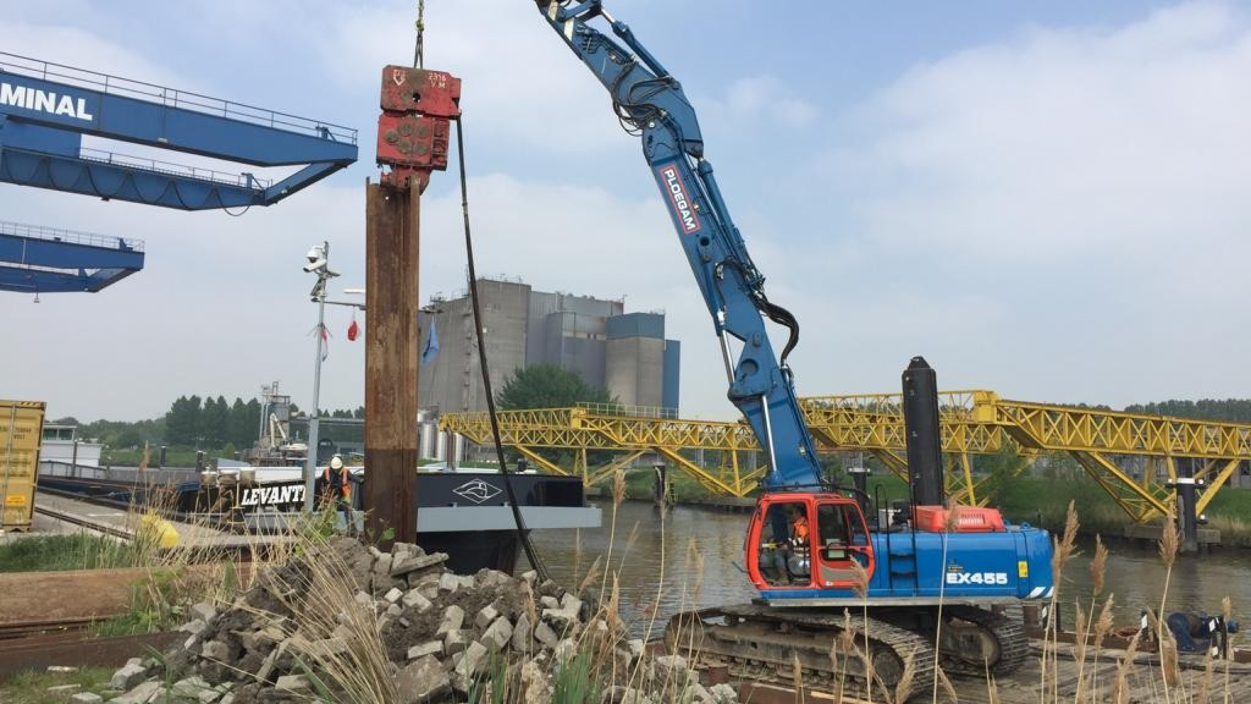 Blauwe Ploegam kraan hijst damwand vanaf een ponton in het water