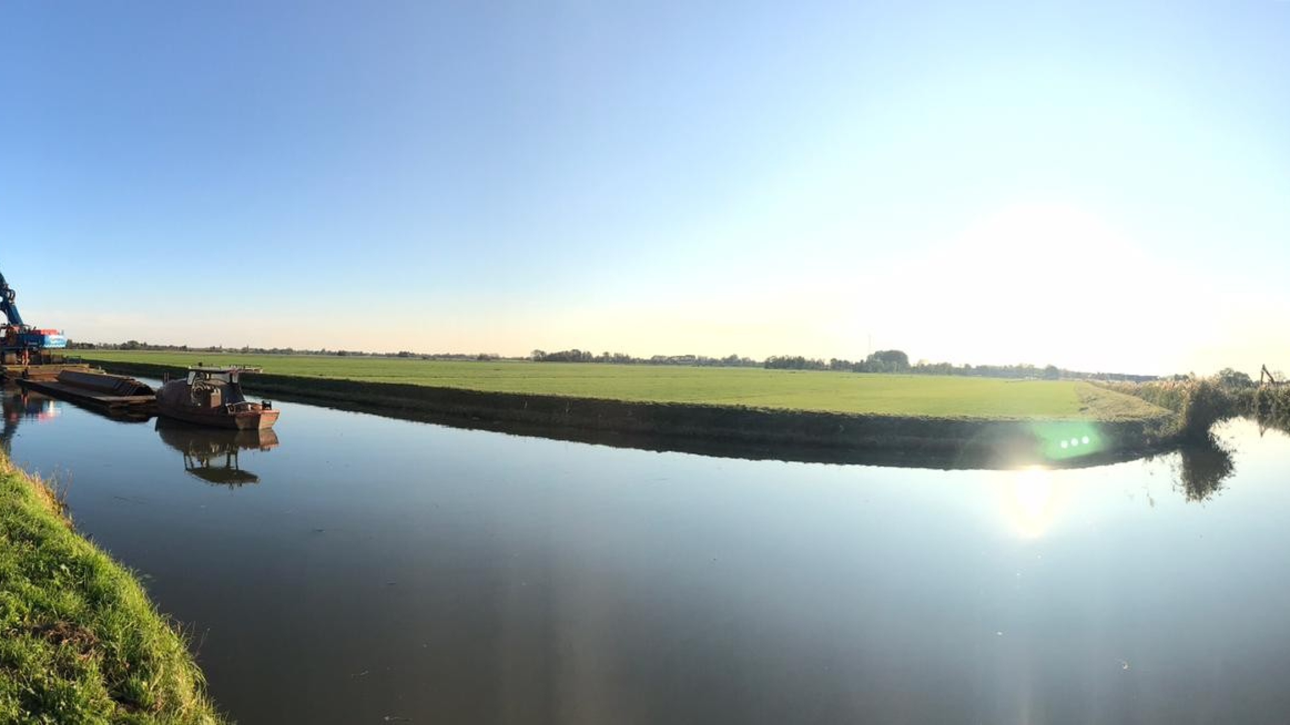 Rivier met groen gras aan de overkant en een laaghangde zon