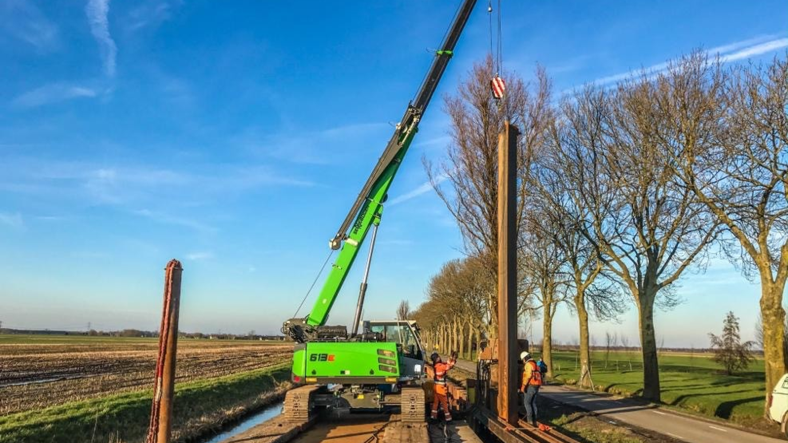 Werkzaamheden met damwanden bij de Montfortsekade met groene kraan vanaf ponton op het water