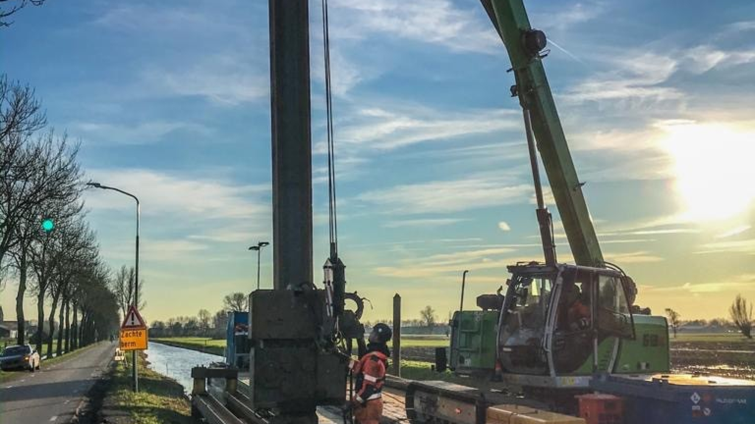 Groene kraan hijst vanaf ponton op het water damwanden in de Montfoortsevaartkade