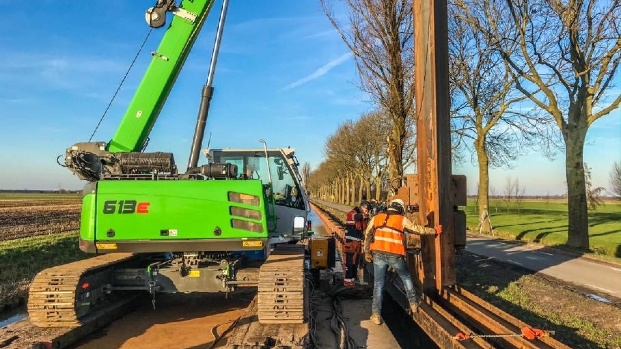 Groene kraan hijst vanaf ponton op het water damwanden in de Montfoortsevaartkade