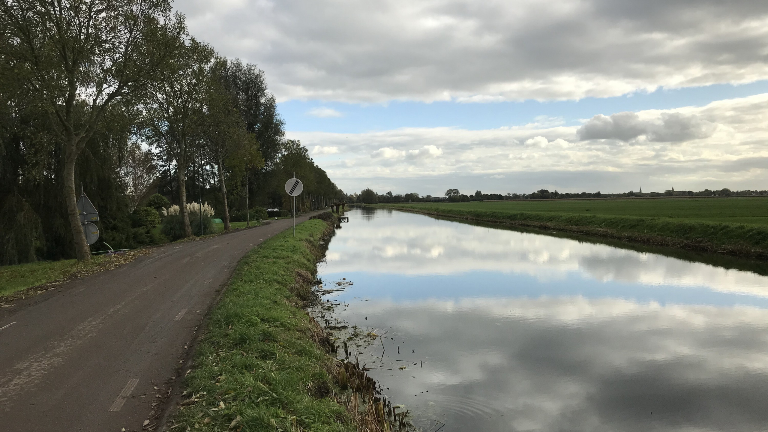 Rivier met een weg ernaast met een verkeersbord en groene berm