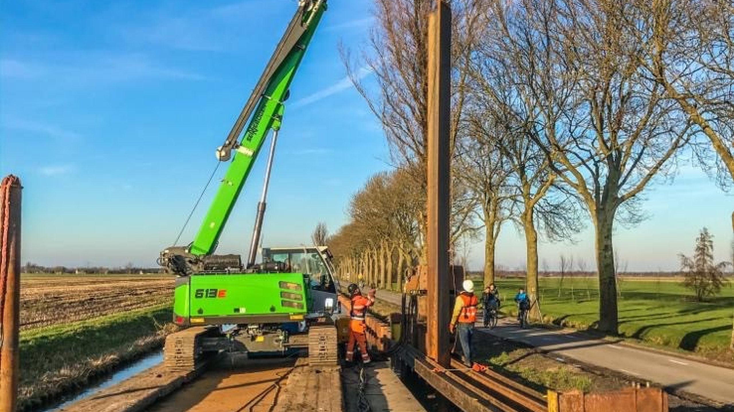 Groene kraan hijst vanaf ponton op het water damwanden in de Montfoortsevaartkade