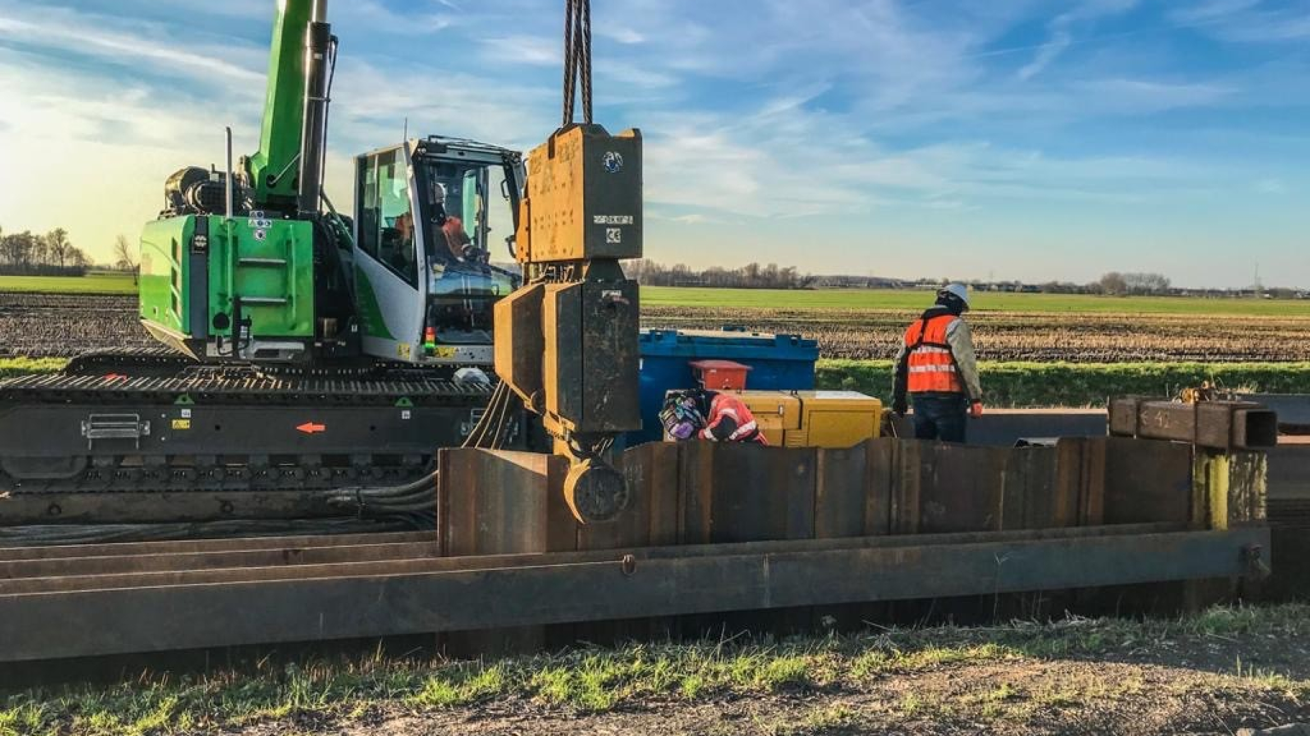 Groene kraan hijst vanaf ponton op het water damwanden in de Montfoortsevaartkade