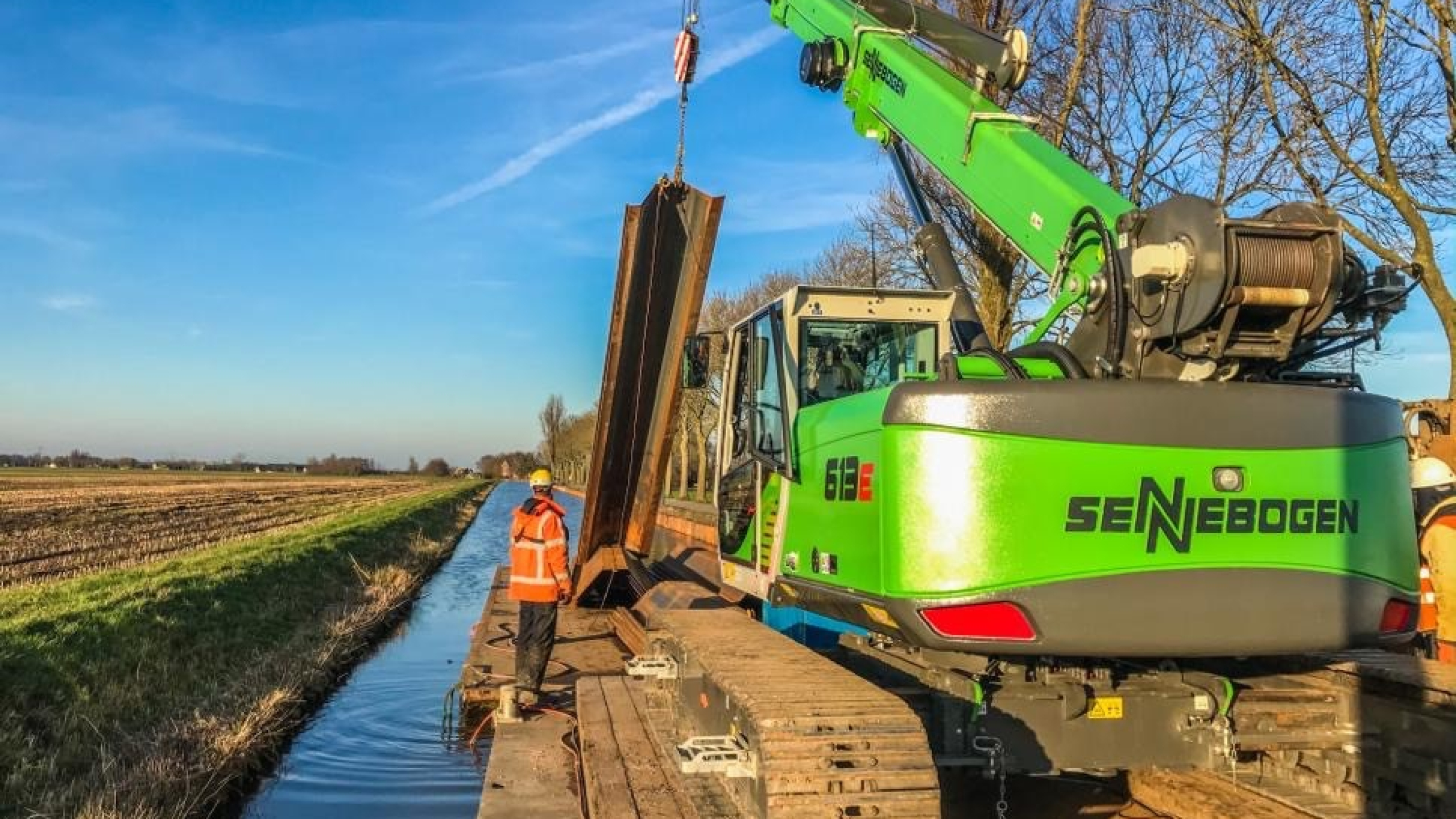 Groene kraan hijst vanaf ponton op het water damwanden in de Montfoortsevaartkade