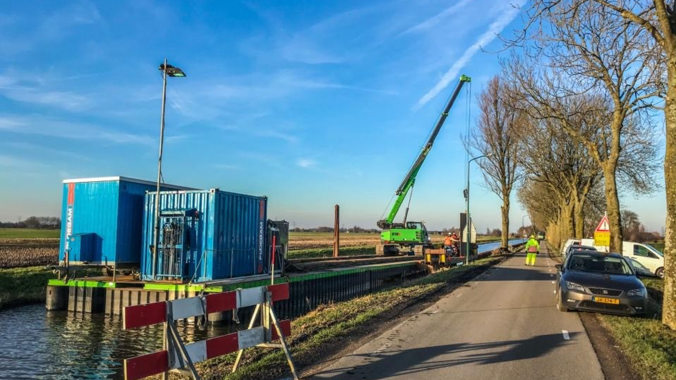 Groene kraan hijst vanaf ponton op het water damwanden in de Montfoortsevaartkade