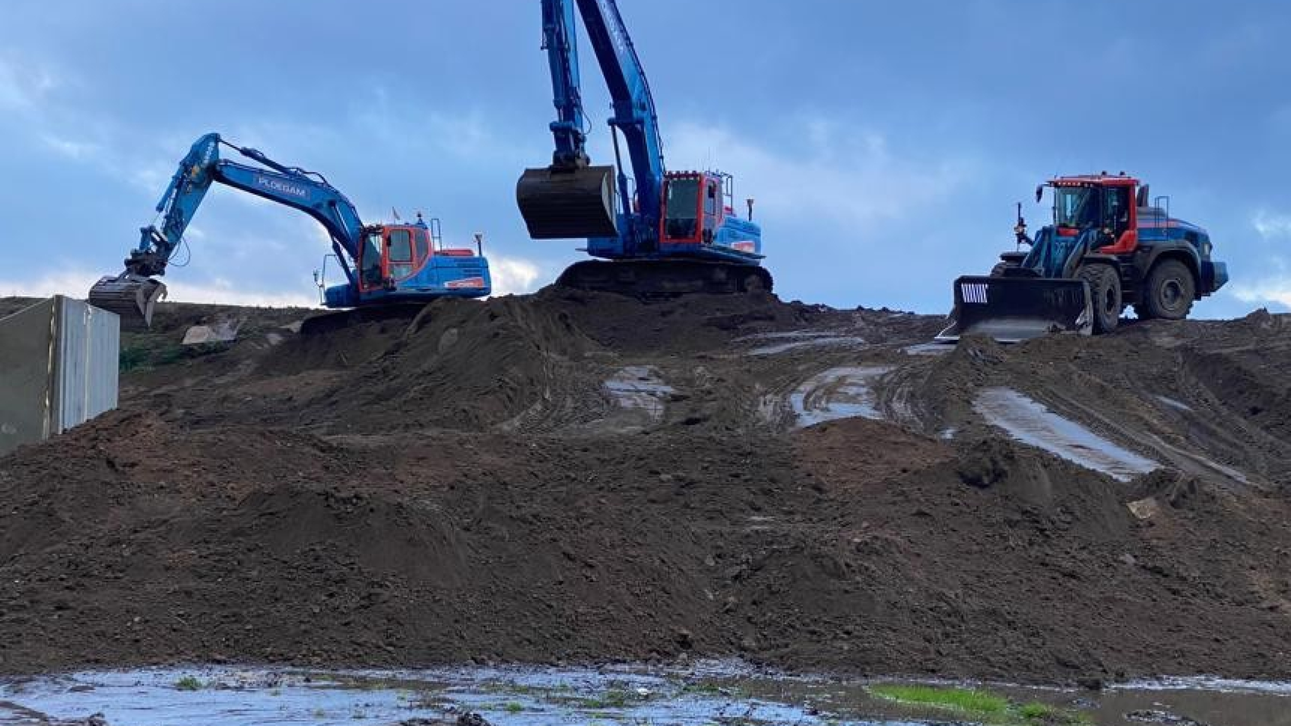 Twee Ploegam kranen en een shovel aan het werk op een berg van zand