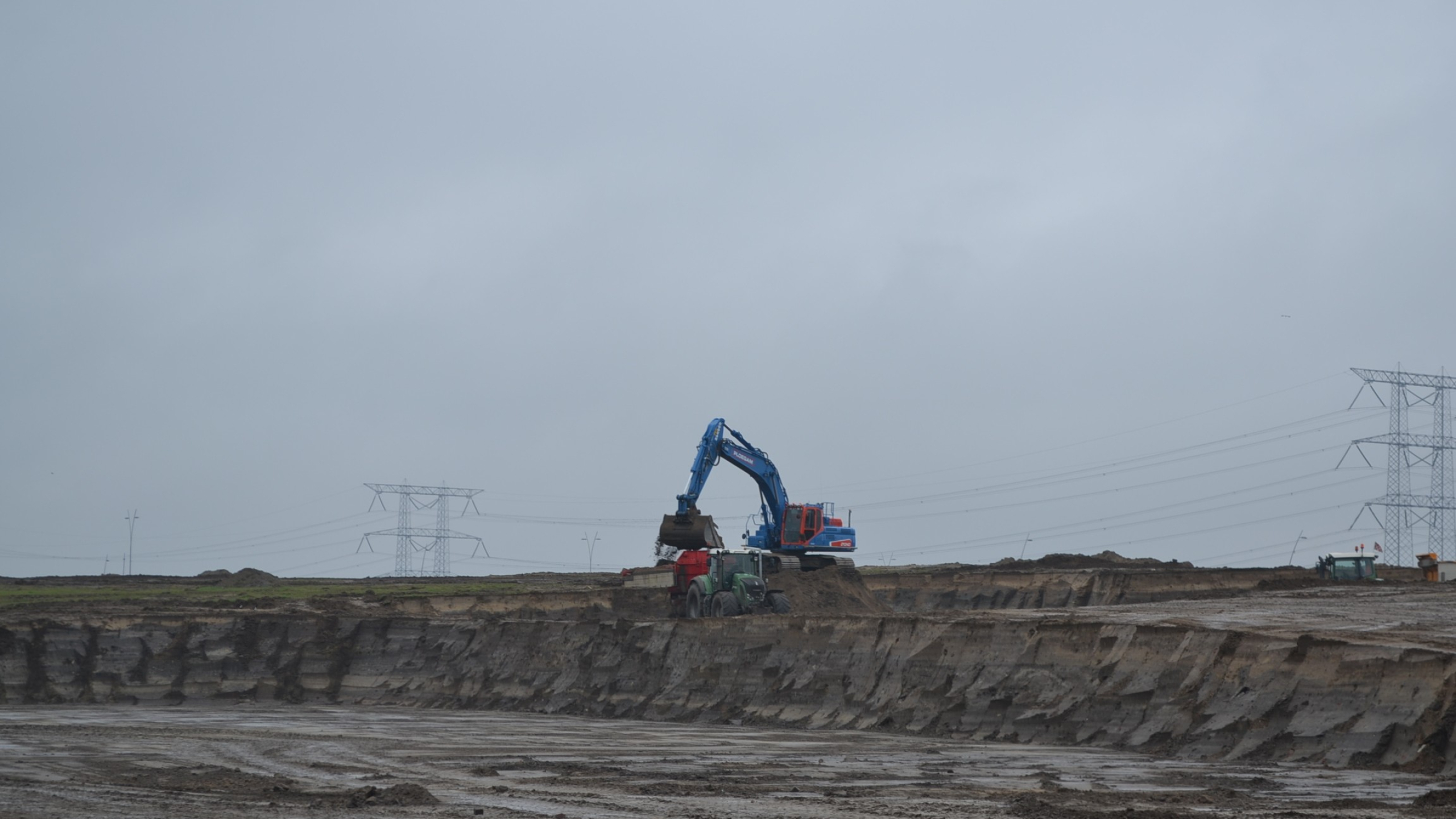 Blauwe Ploegam kraan schept zand in de bak van een tractor