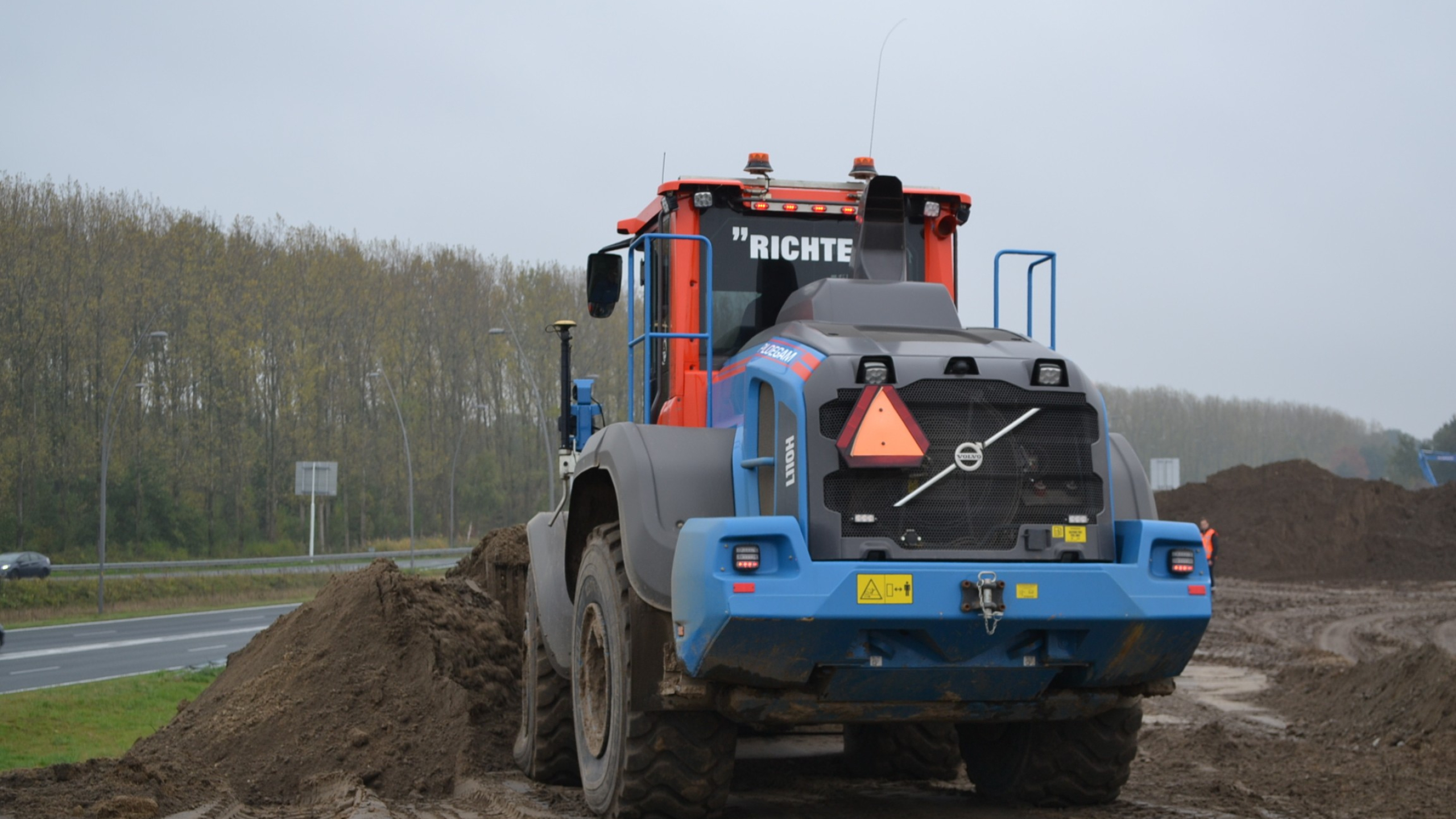 Achterkant van een Ploegam shovel aan het werk in het zand naast een weg