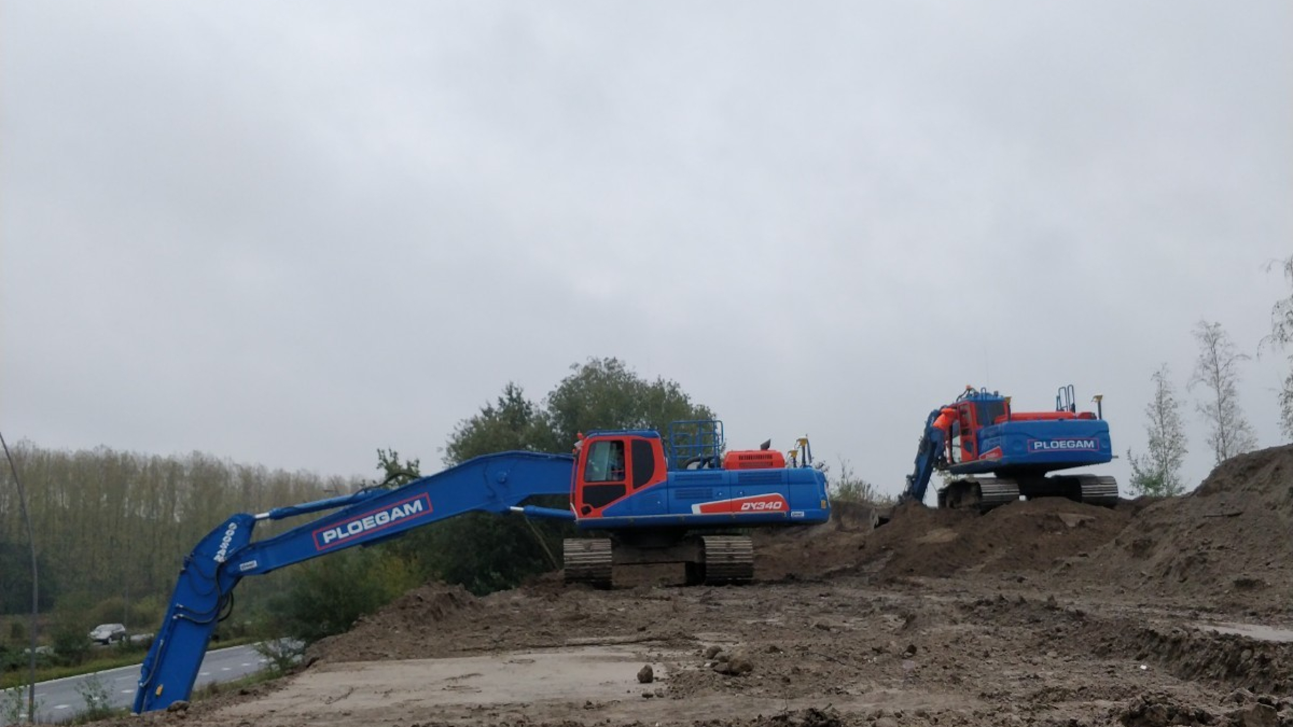 Twee blauwe ploegam kranen aan het werk in het zand op een grijze dag