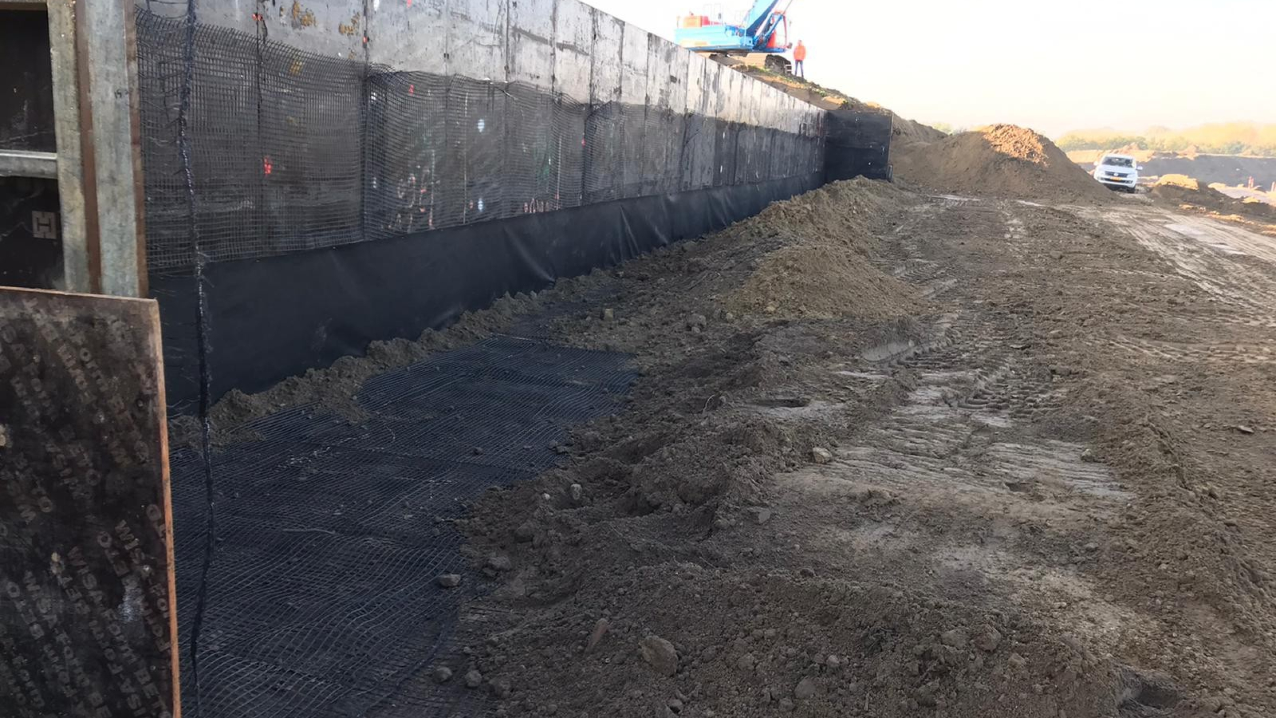 Zand op een bouwplaats met een blauwe kraan en witte auto op de achtergrond