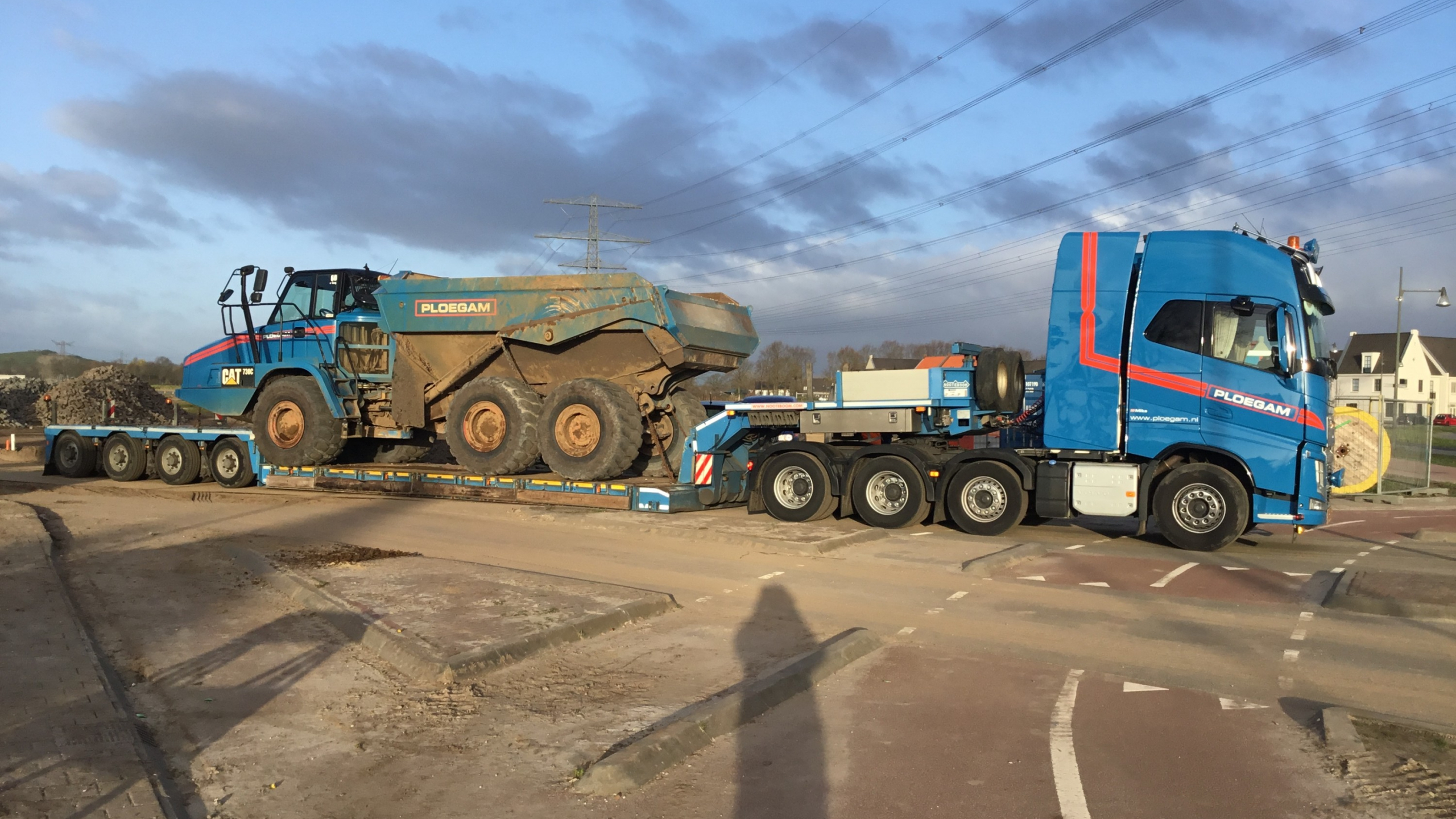 Blauwe Ploegam vrachtwagen vervoert machine over straat