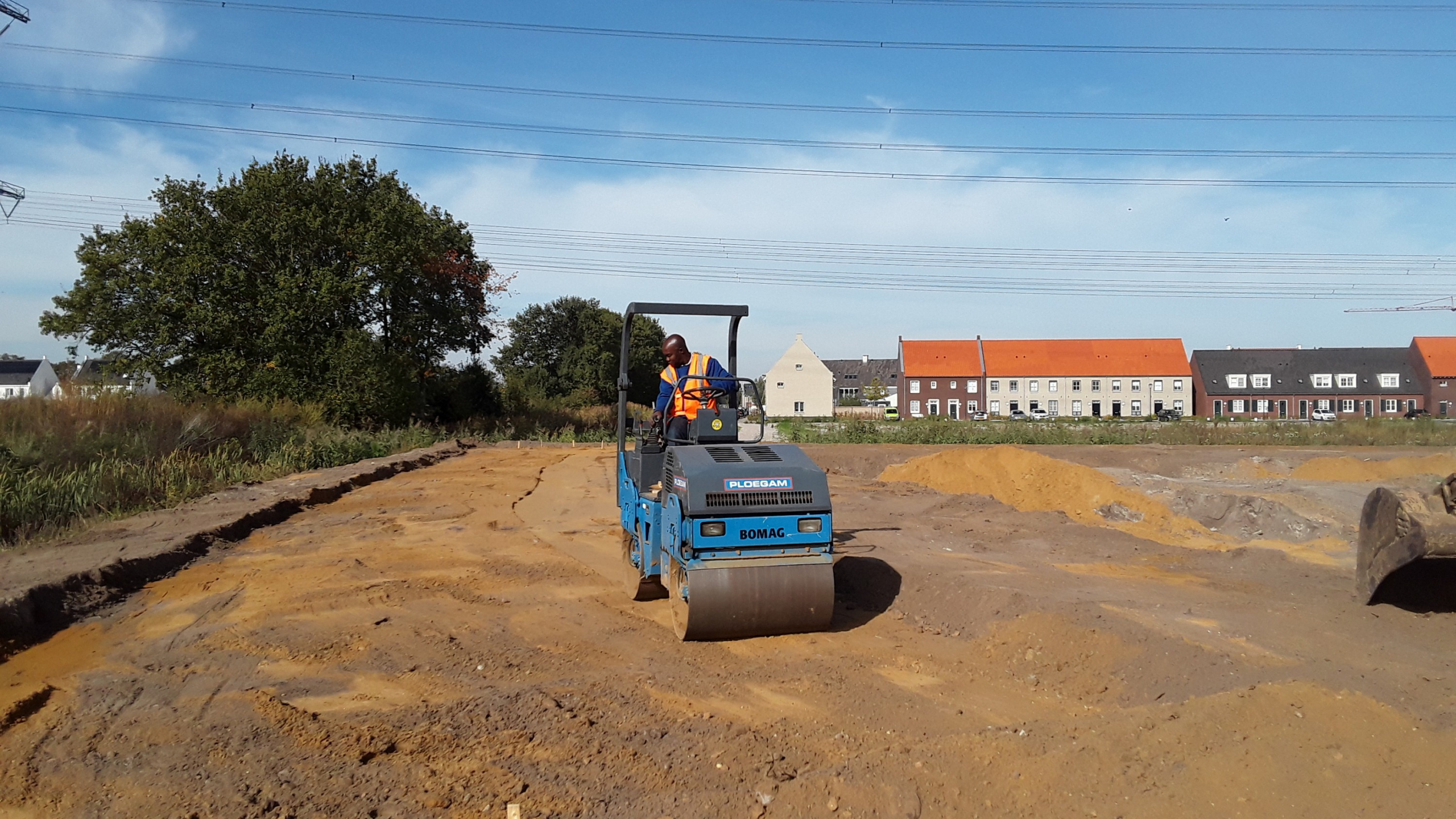 Man met veiligheidshesje zit in machine om zand te egaliseren