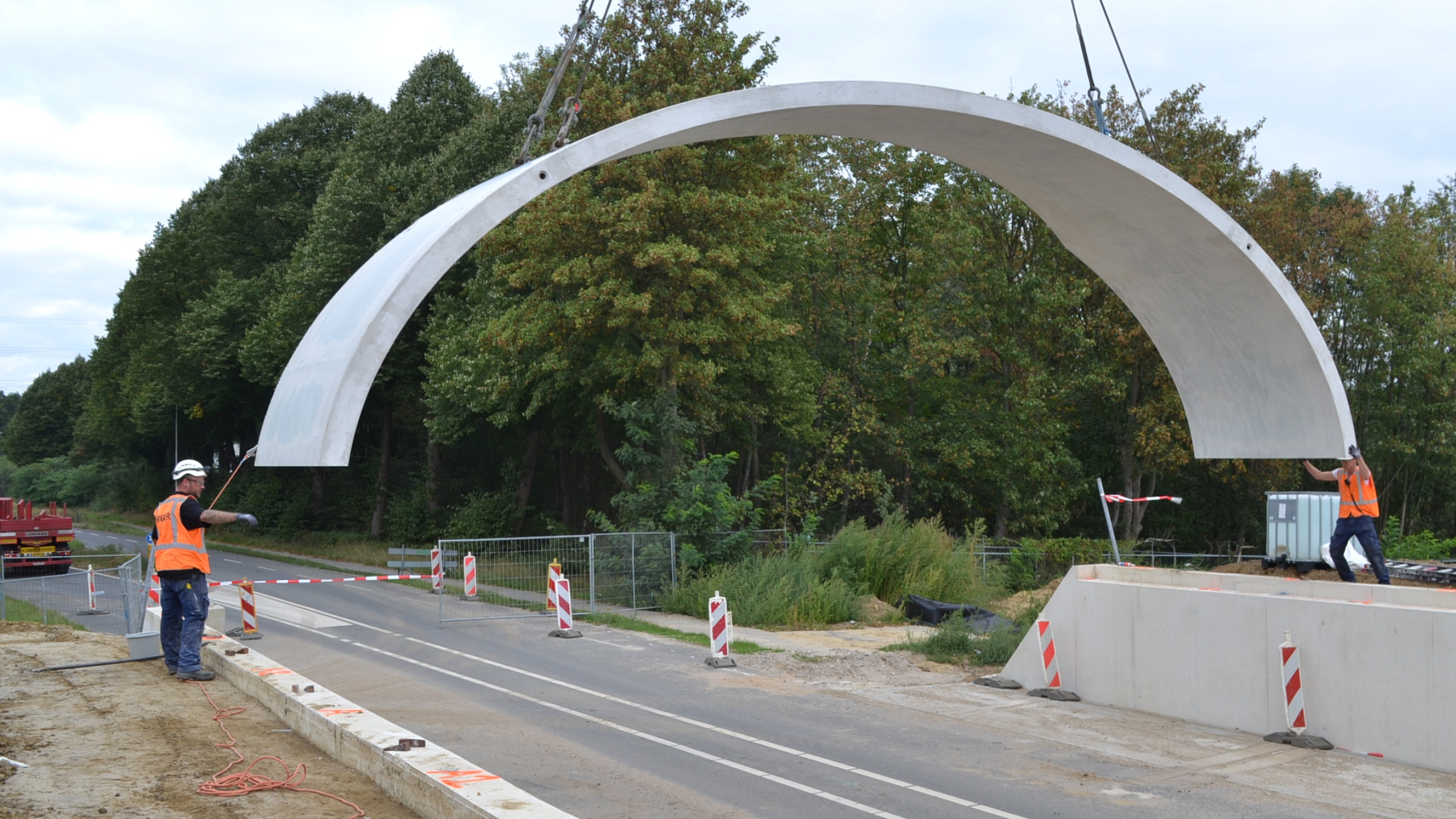Twee mannen met veiligheidshesjes plaatsen betonnen koepel bij ecoduct