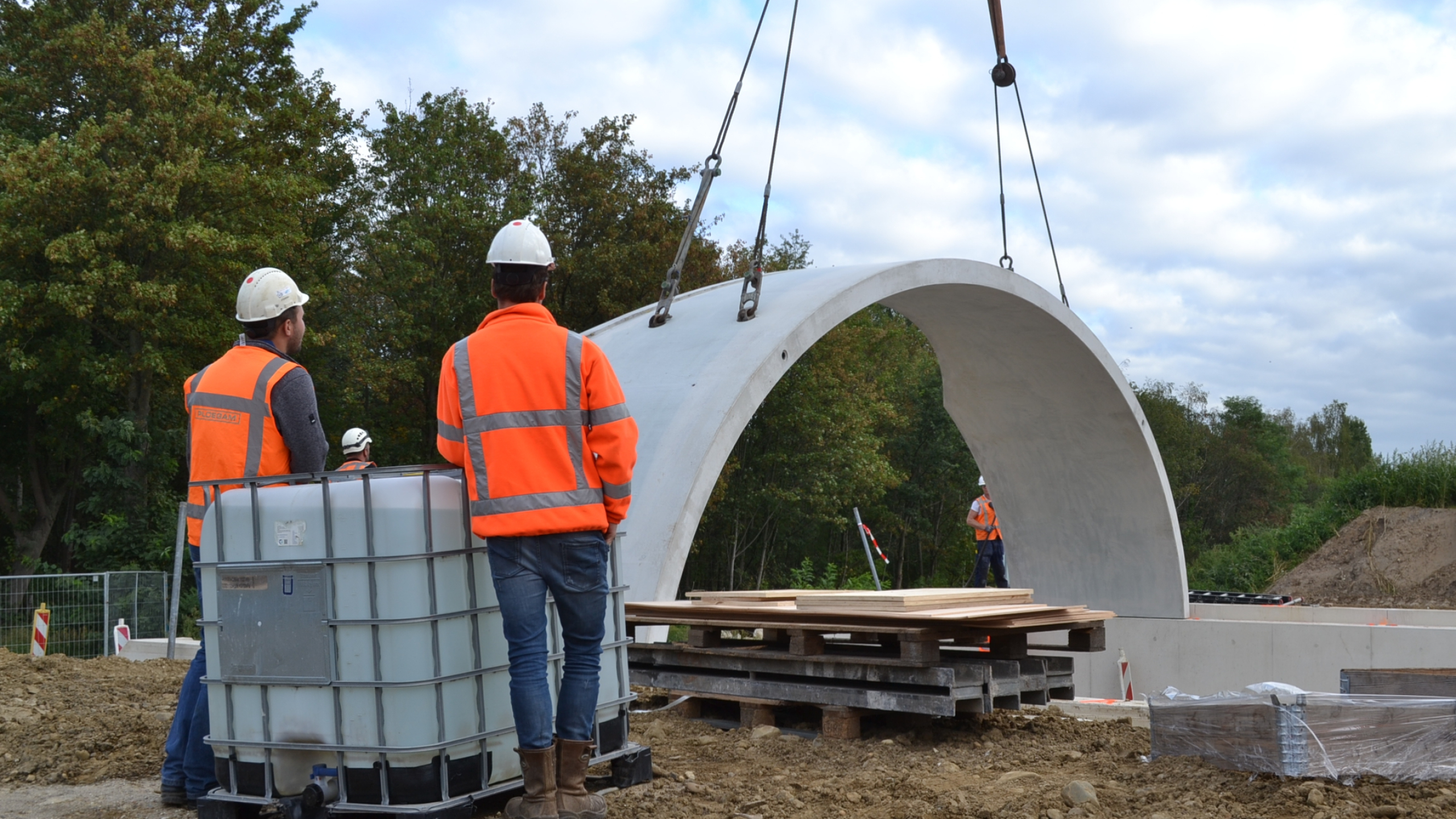 Mannen met veiligheidshesjes en helmen kijken toe bij het plaatsen van een betonnen koepel
