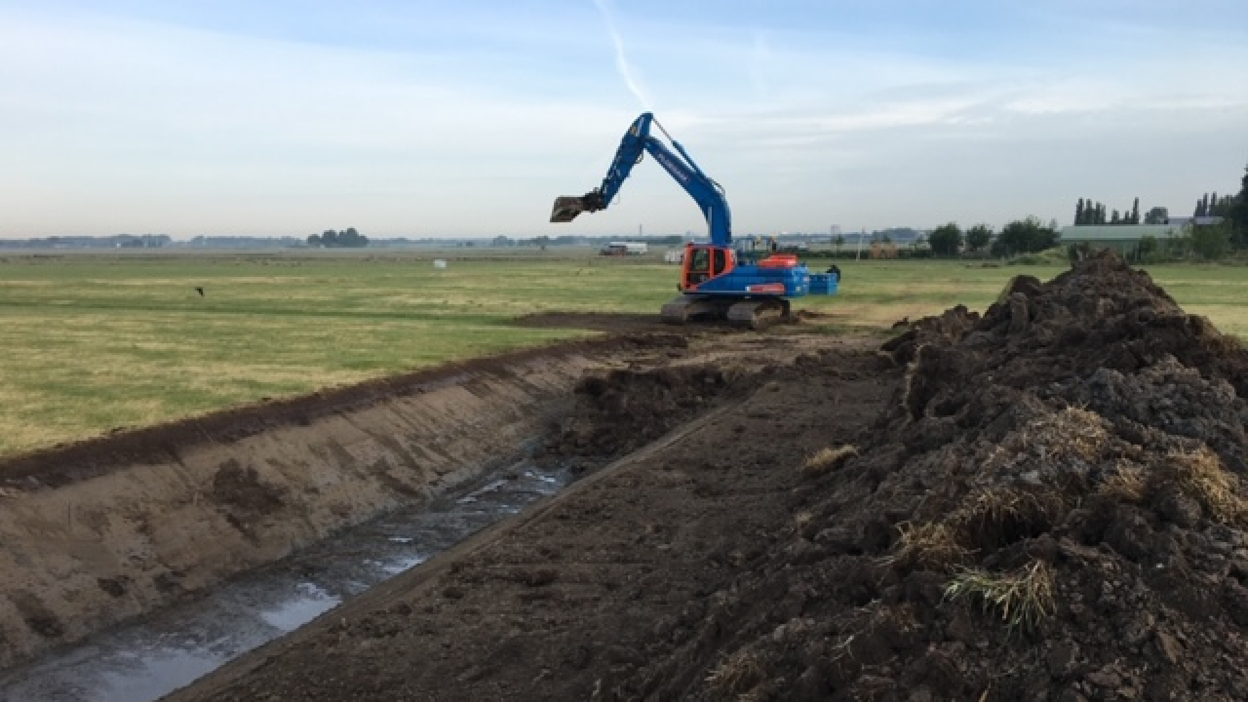 Blauwe Ploegam kraan op het zand tussen de weilanden graaft een gleuf in de grond
